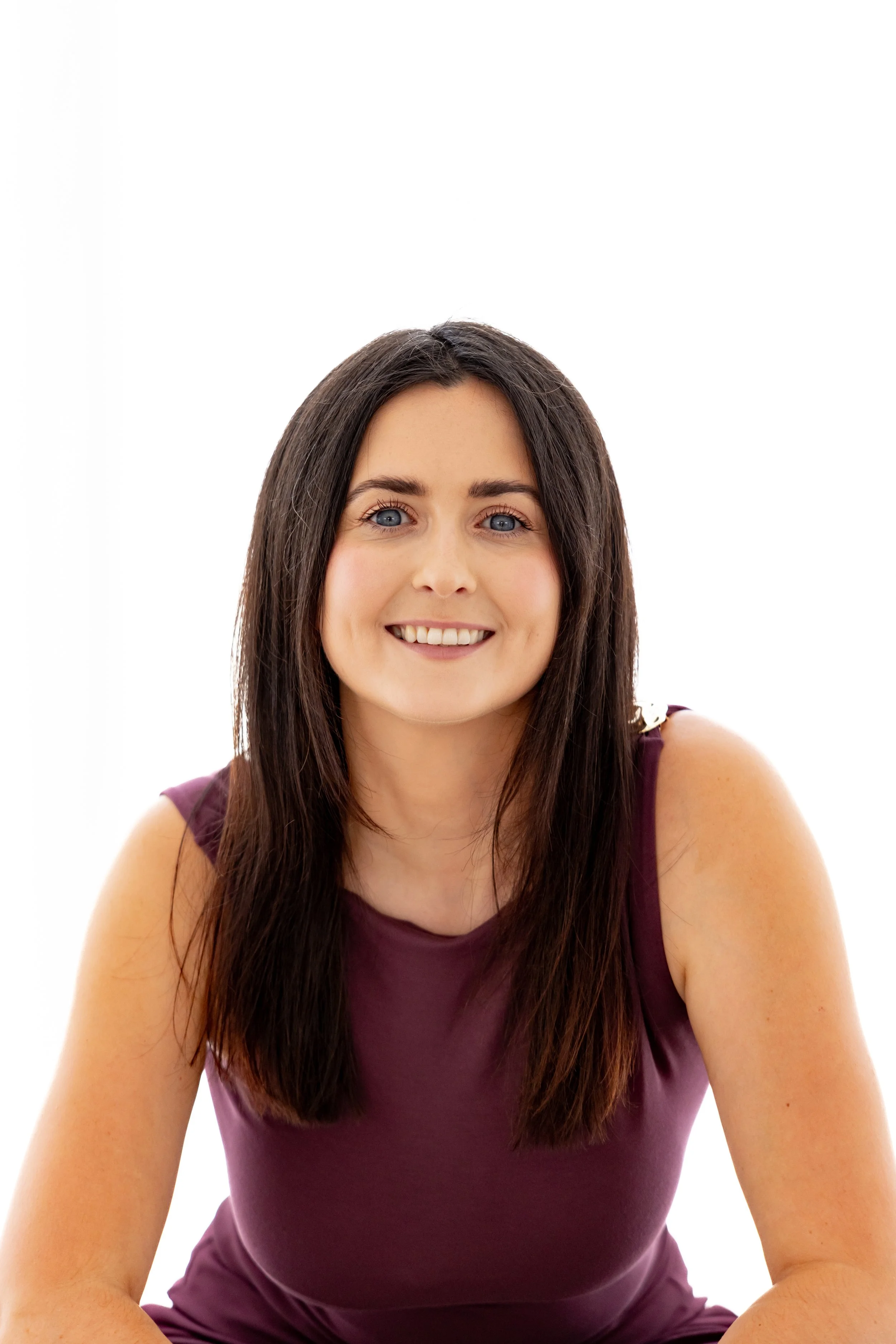 A young woman with long brown hair and blue eyes smiling, wearing a sleeveless burgundy top, against a plain white background.