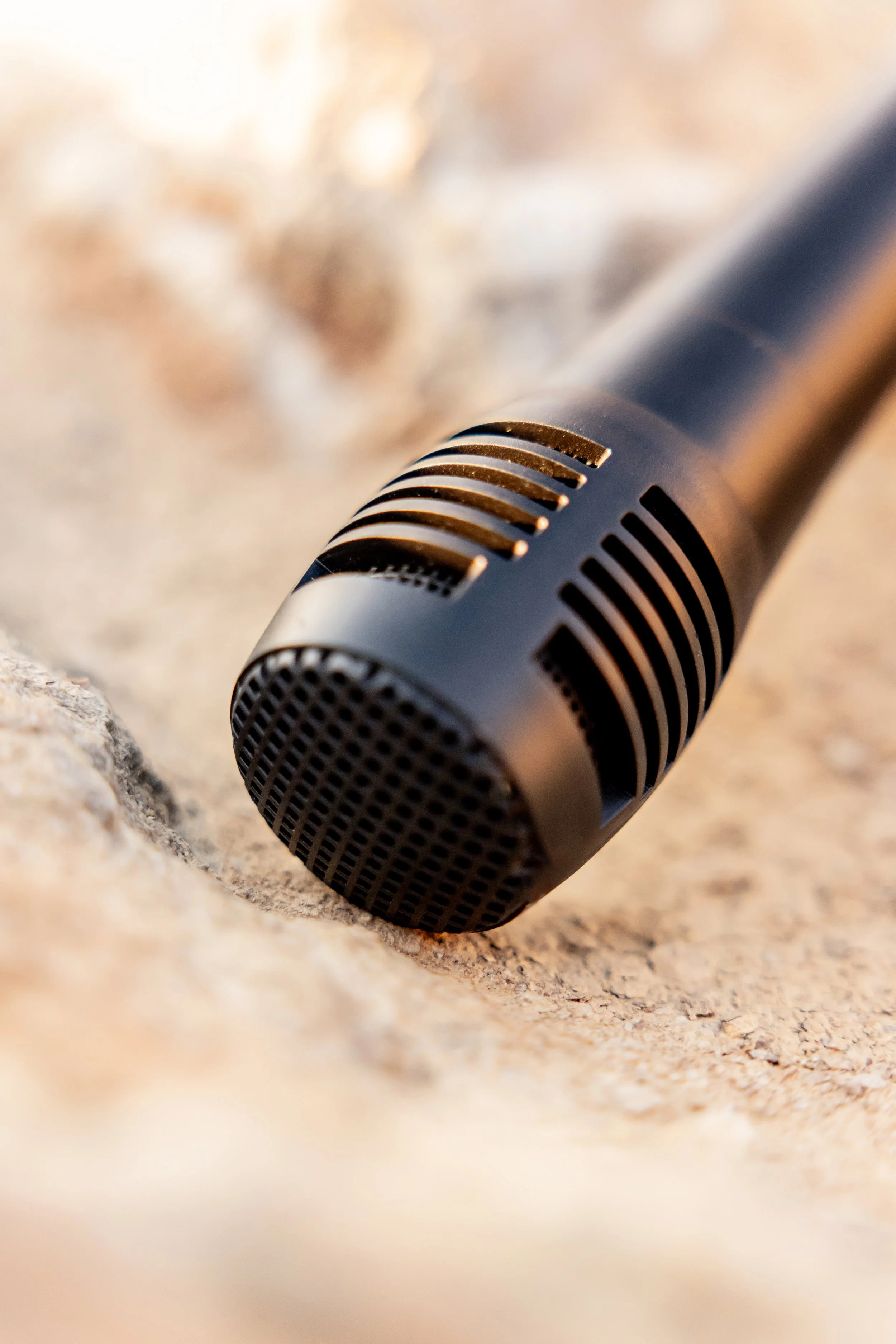Close-up of a black microphone with a metal grille lying on a textured surface, with a blurred background.