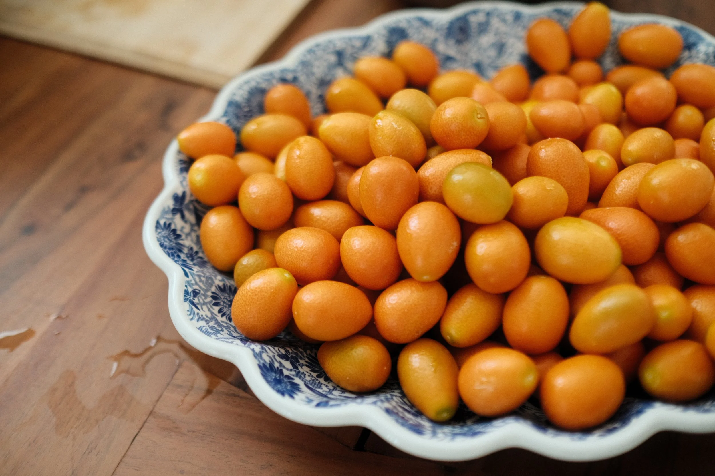 A bowl filled with small, round, orange kumquats on a wooden table.