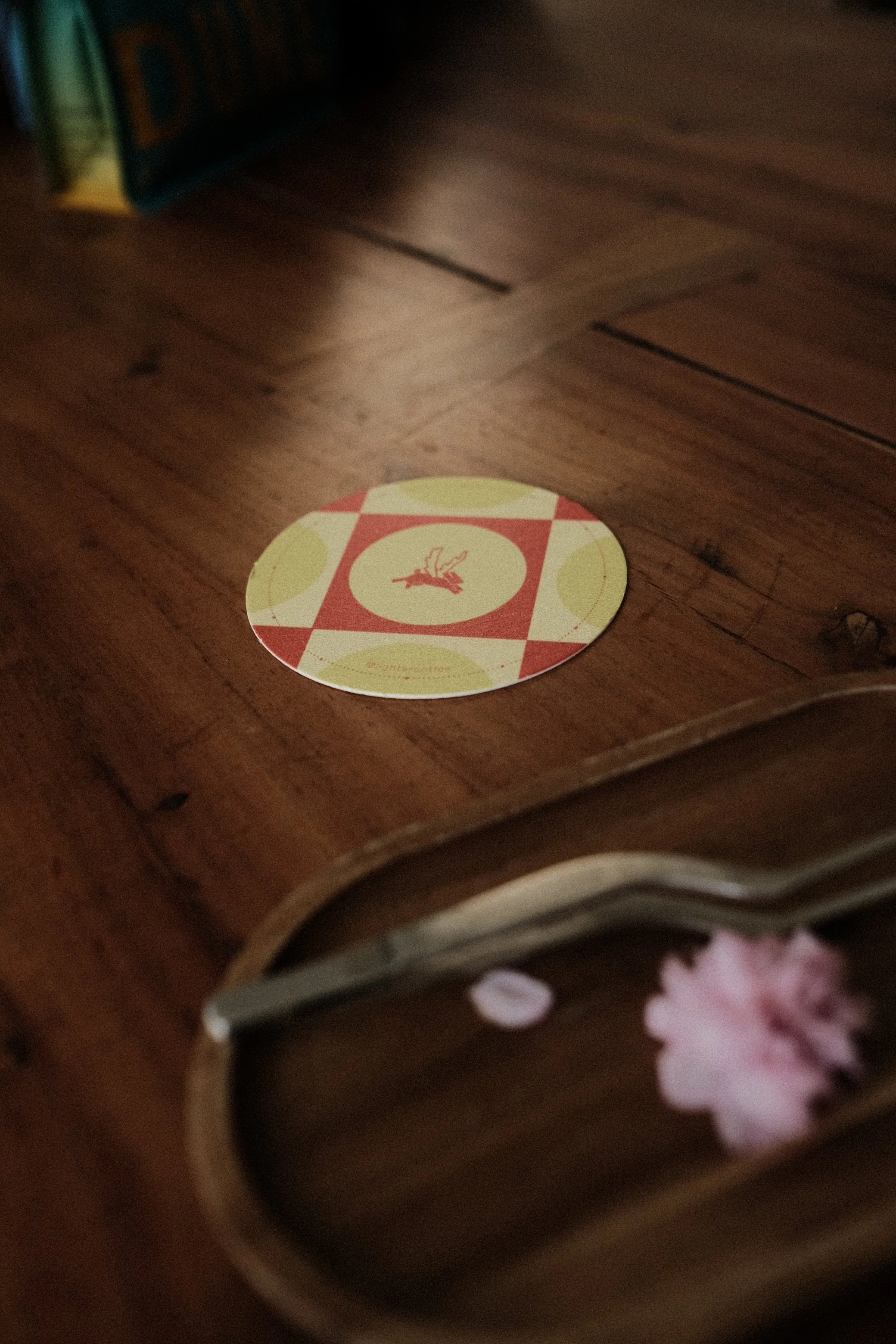 A round sticker on a wooden surface featuring a red and green checkered pattern with a stylized bird in the center.