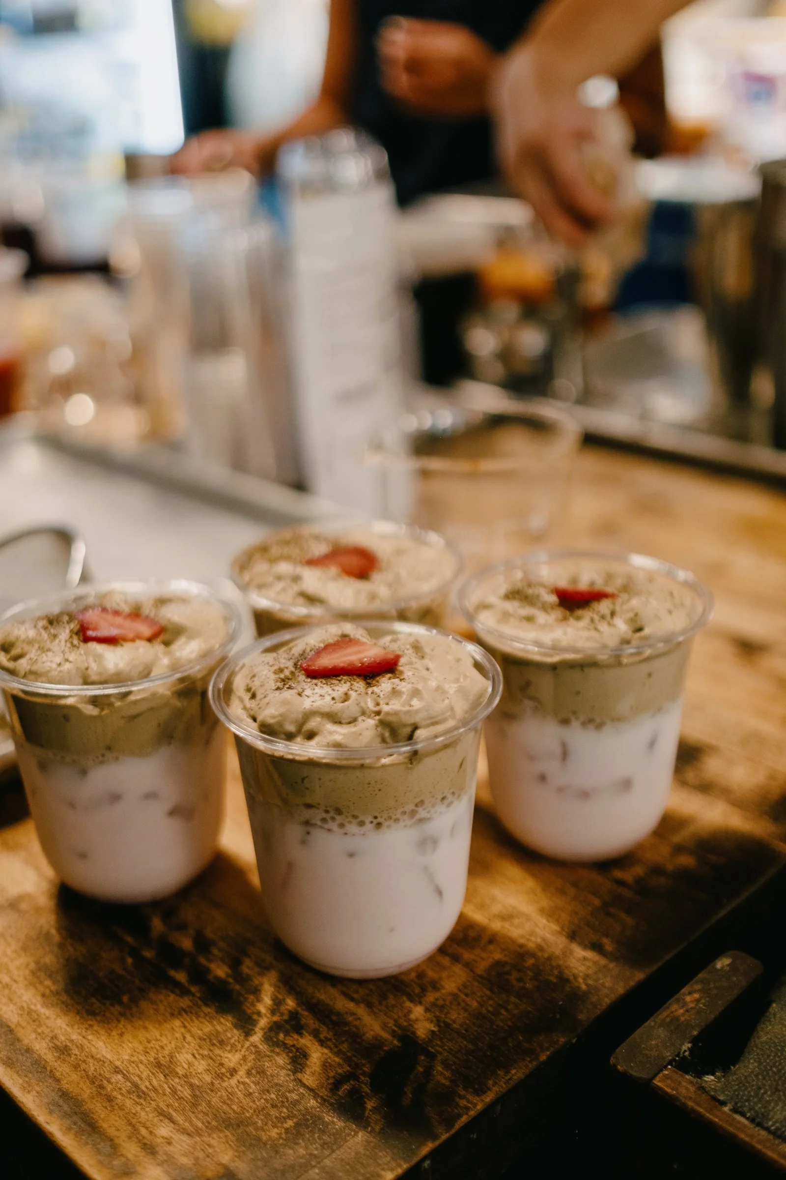 Creamy dessert cups topped with sliced strawberries and hojicha powder on a wooden surface.