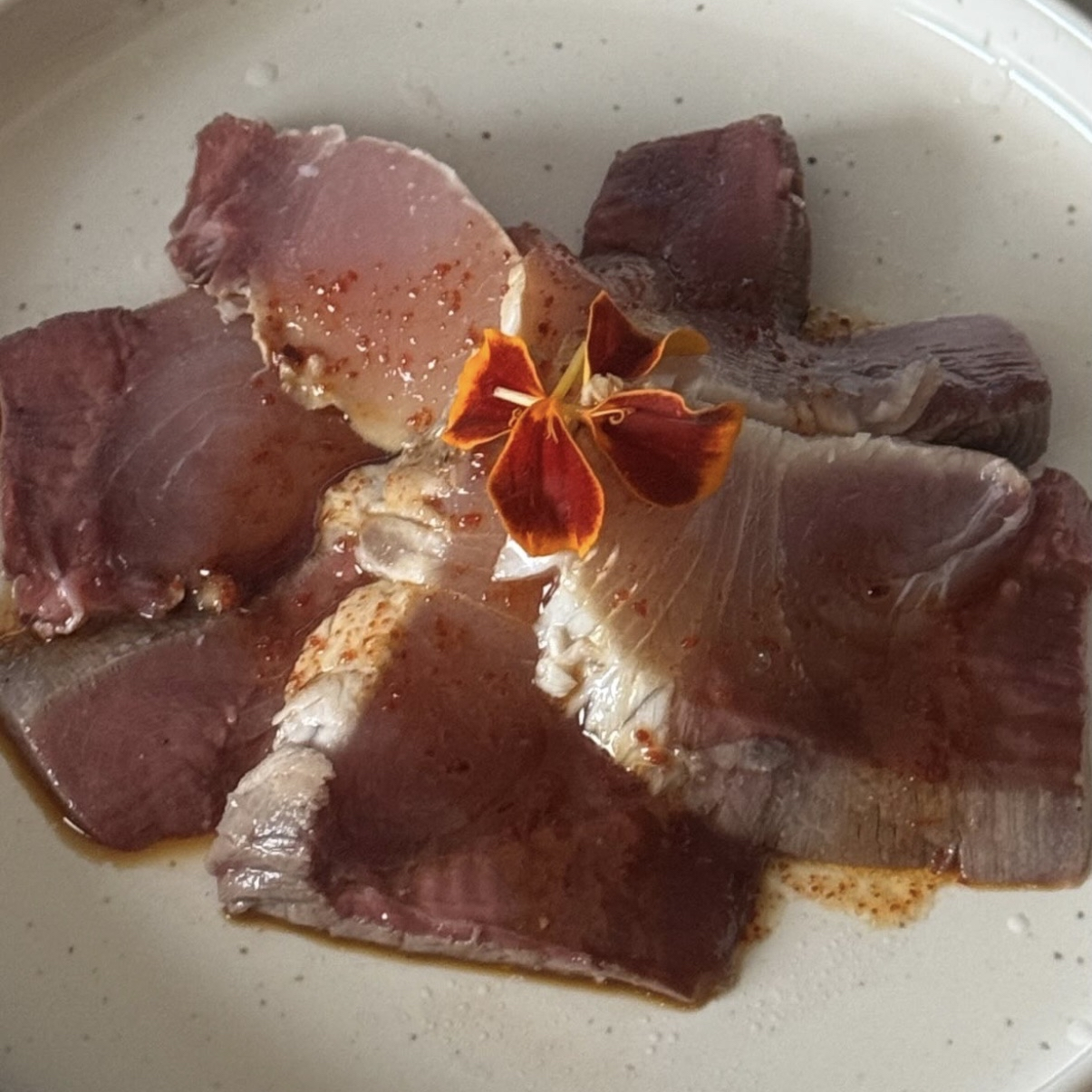 Raw pieces of meat with reddish-brown color and a flower garnish in the center.