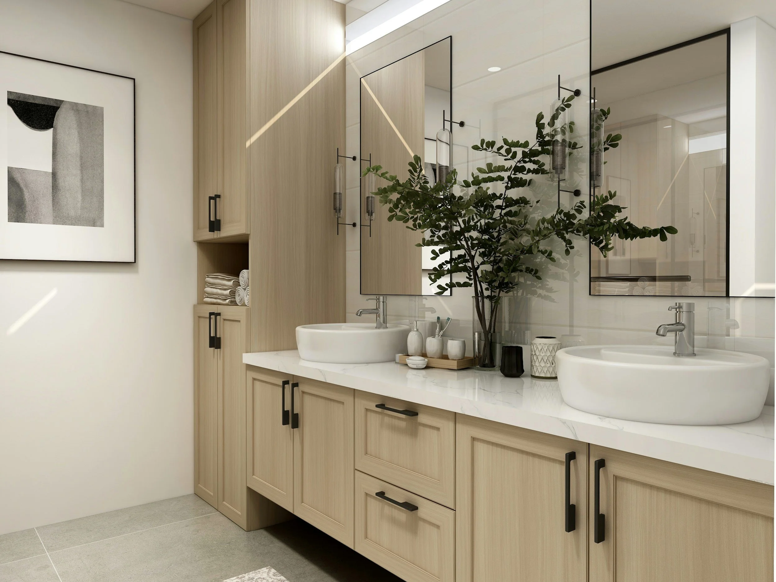 A modern bathroom vanity with light wood cabinets, black handles, and a white marble countertop with two vessel sinks. Above the sinks is a large mirror with a thin black frame, decorated with a tall green plant and small decorative containers. To the left, a framed black-and-white abstract art hangs on the white wall. The floor is covered with light gray tiles.