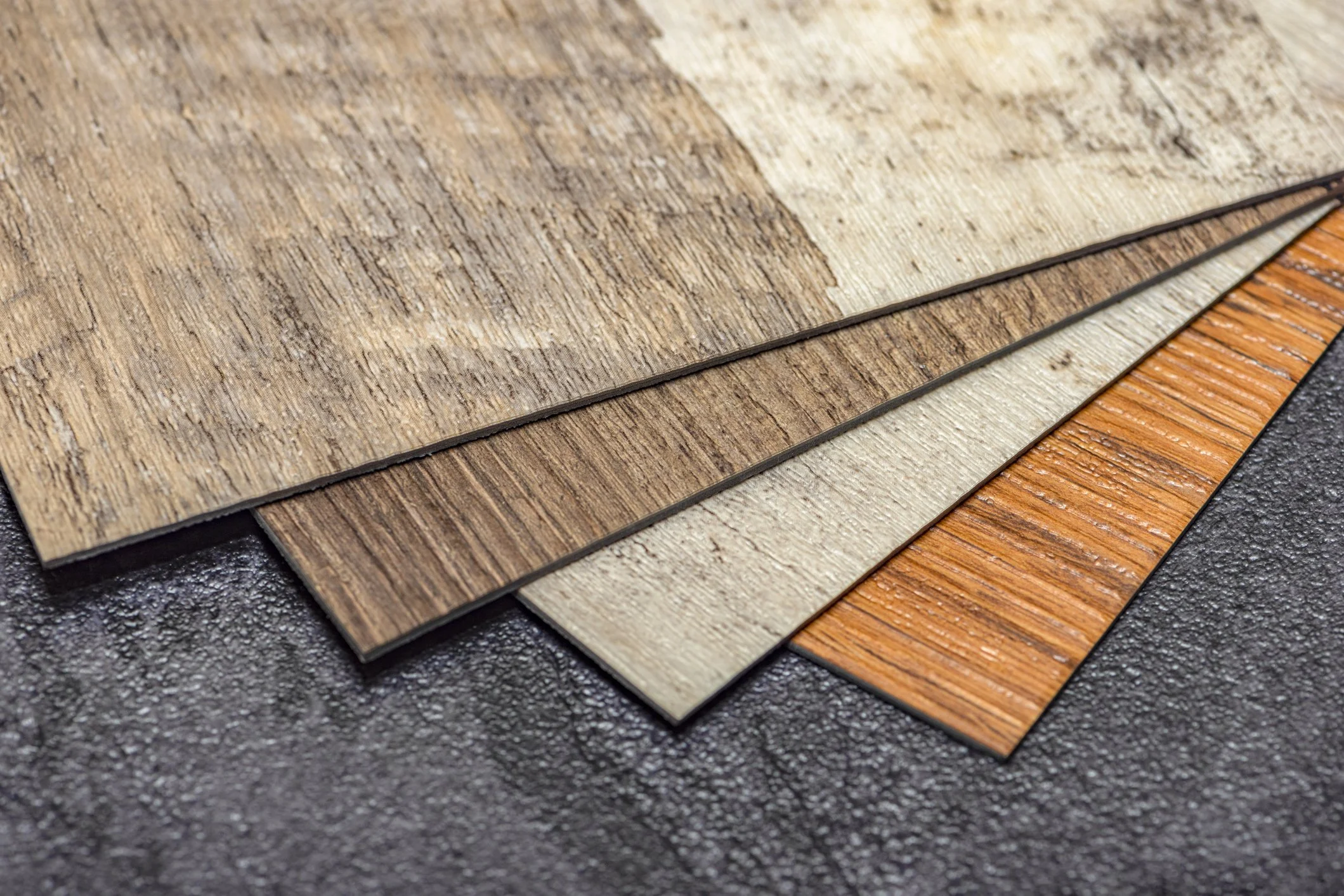 Samples of wood flooring planks in various colors and finishes on a dark textured background.