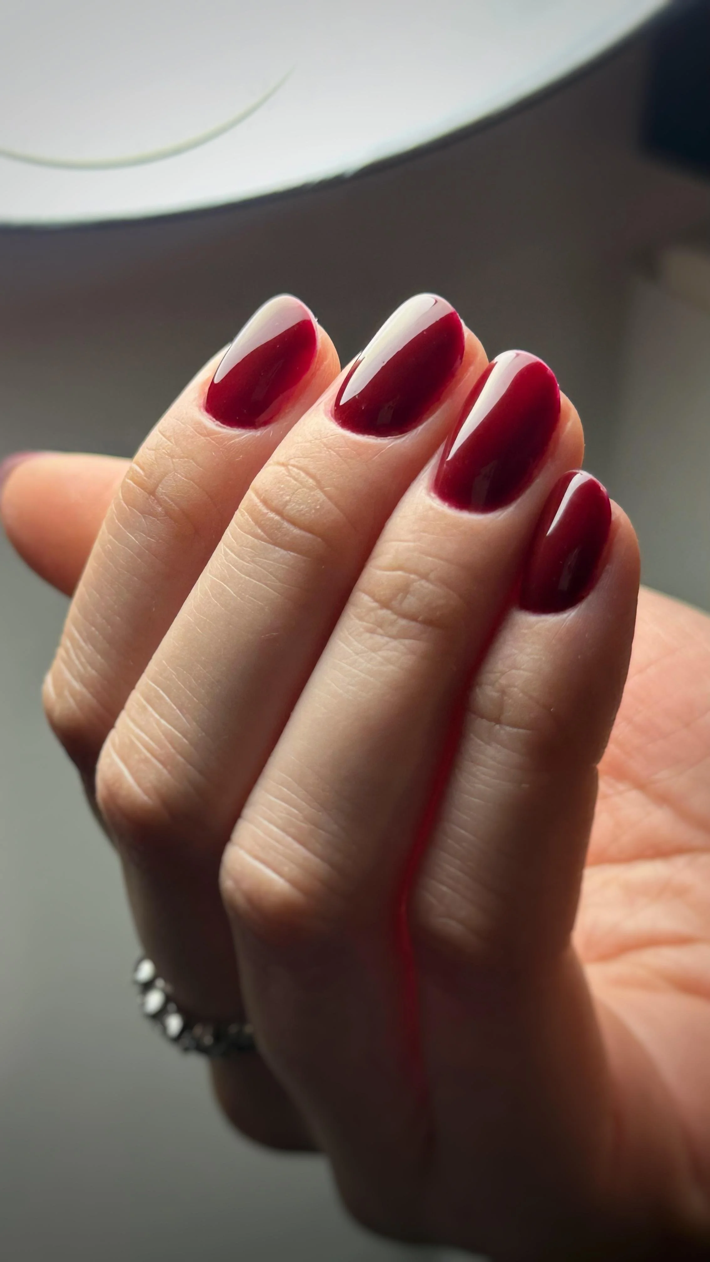 Unghie dipinte di rosso scuro con riflessi lucidi su un dito di una mano.