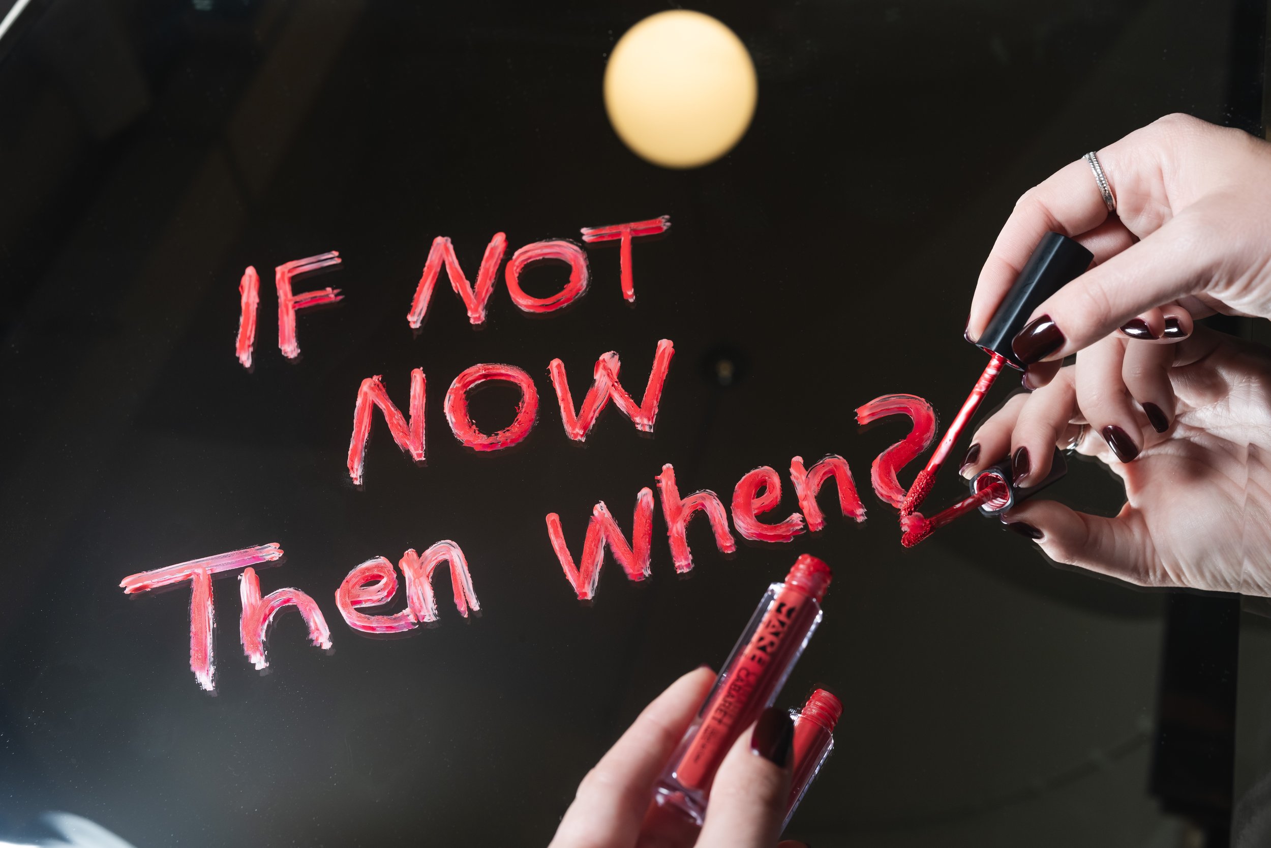 Una persona scrive su una superficie vettoriale con un pennarello rosso che ha scritto 'IF NOT NOW, then when'.