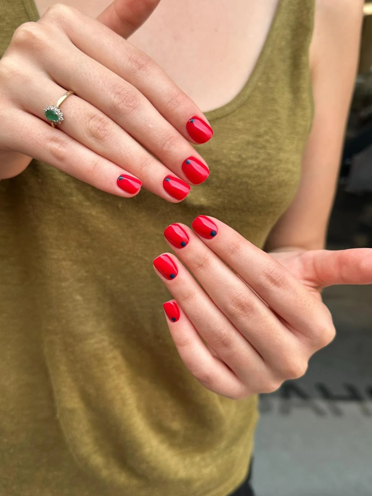 Unghie con smalto rosso con puntini blu e mani con anello con pietra verde