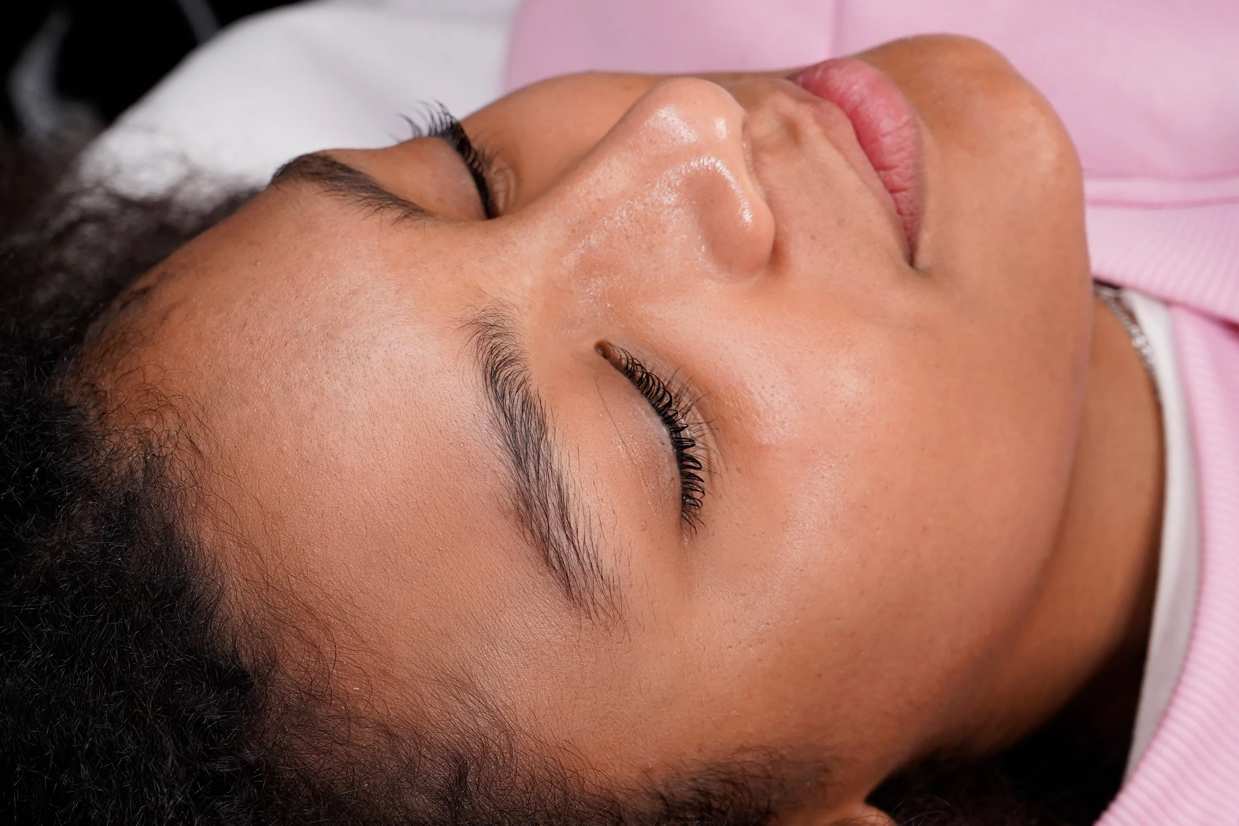 Primo piano di una donna con la pelle liscia e capelli ricci, occhi chiusi, che sembra essere addormentata o in uno stato di relax.