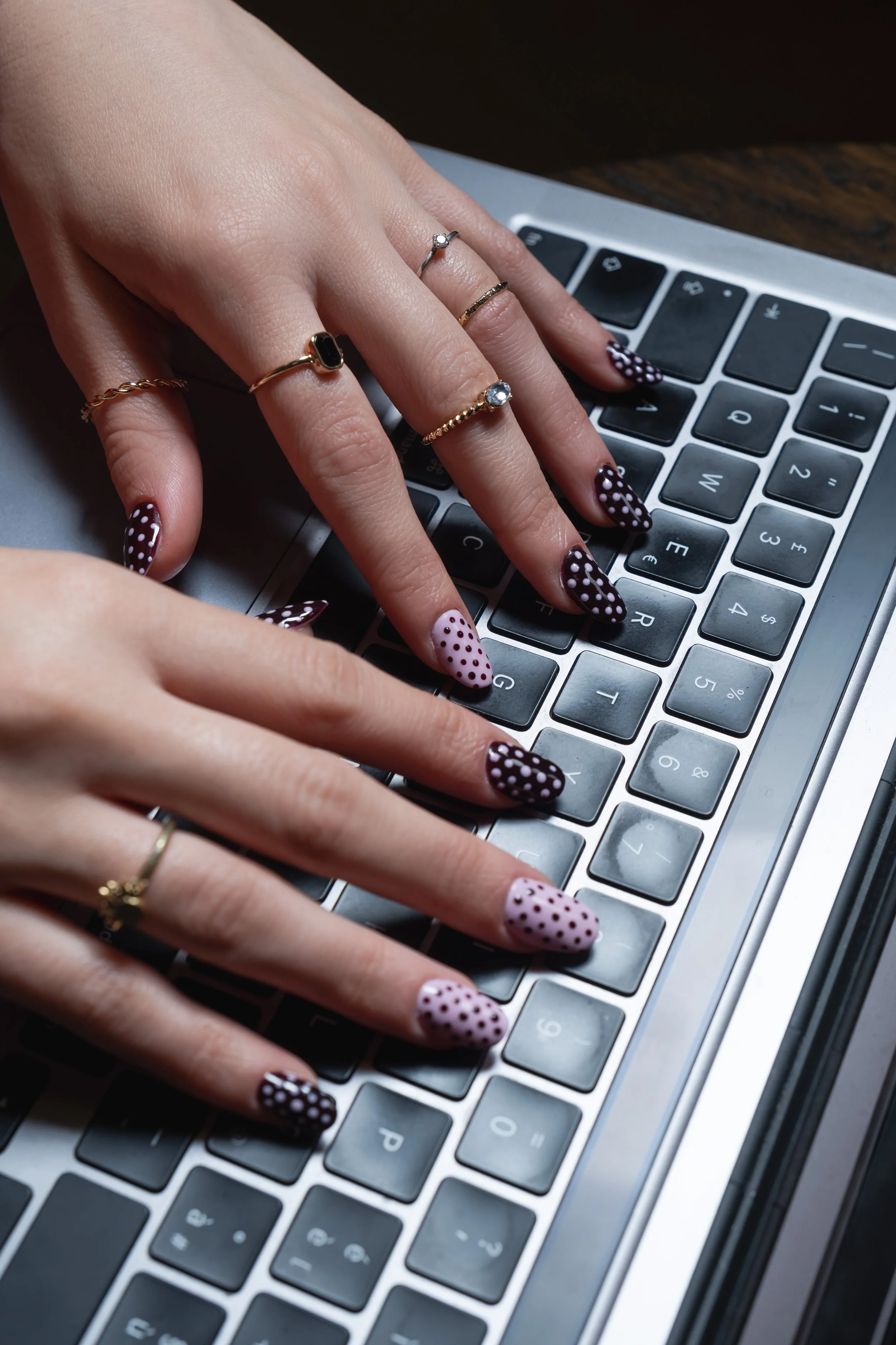 Mani con unghie a pois che premono i tasti di una tastiera di un computer portatile.