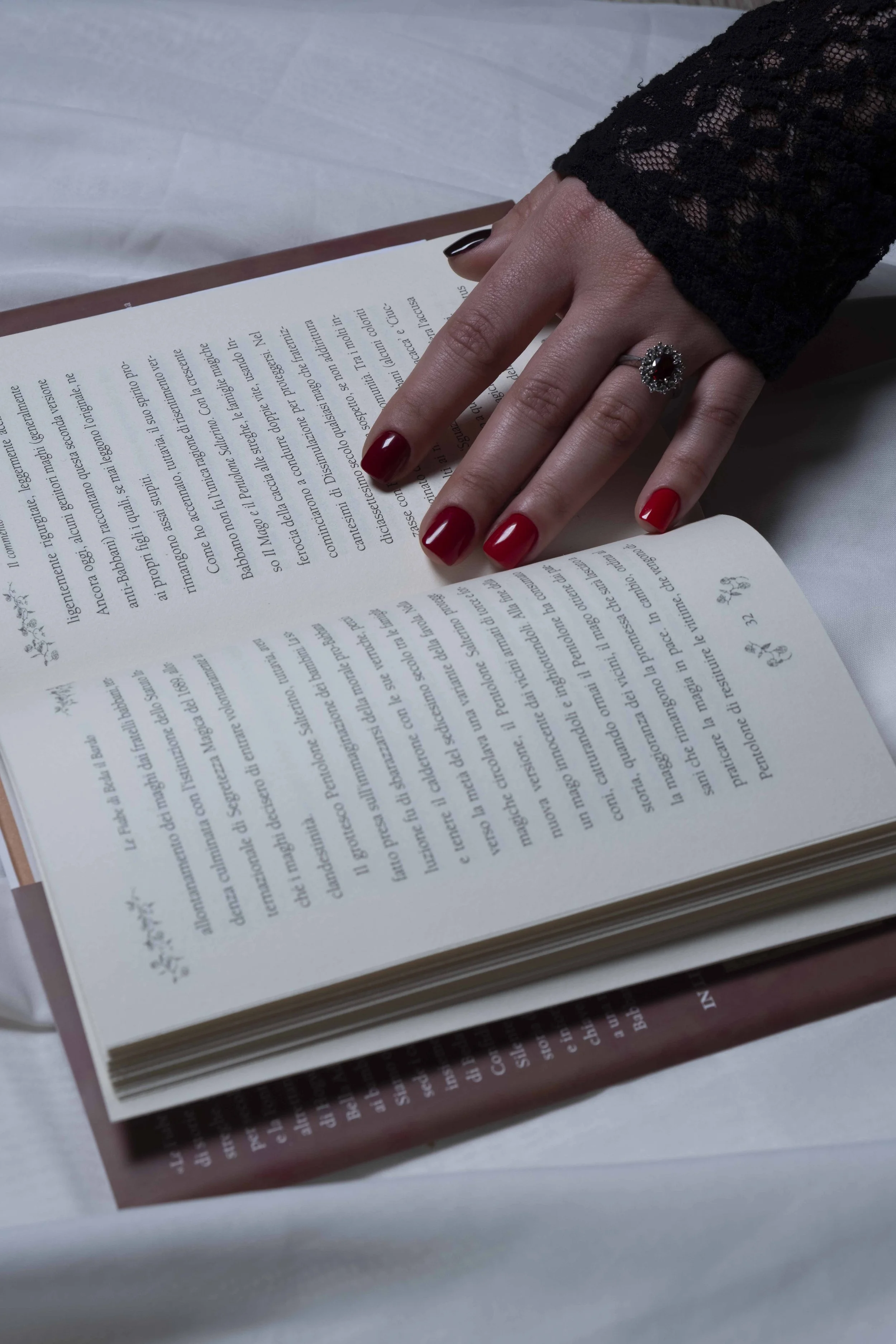 Un libro aperto con una mano femminile con un anello con pietra rossa e smalto rosso sulle unghie, che tiene il libro.