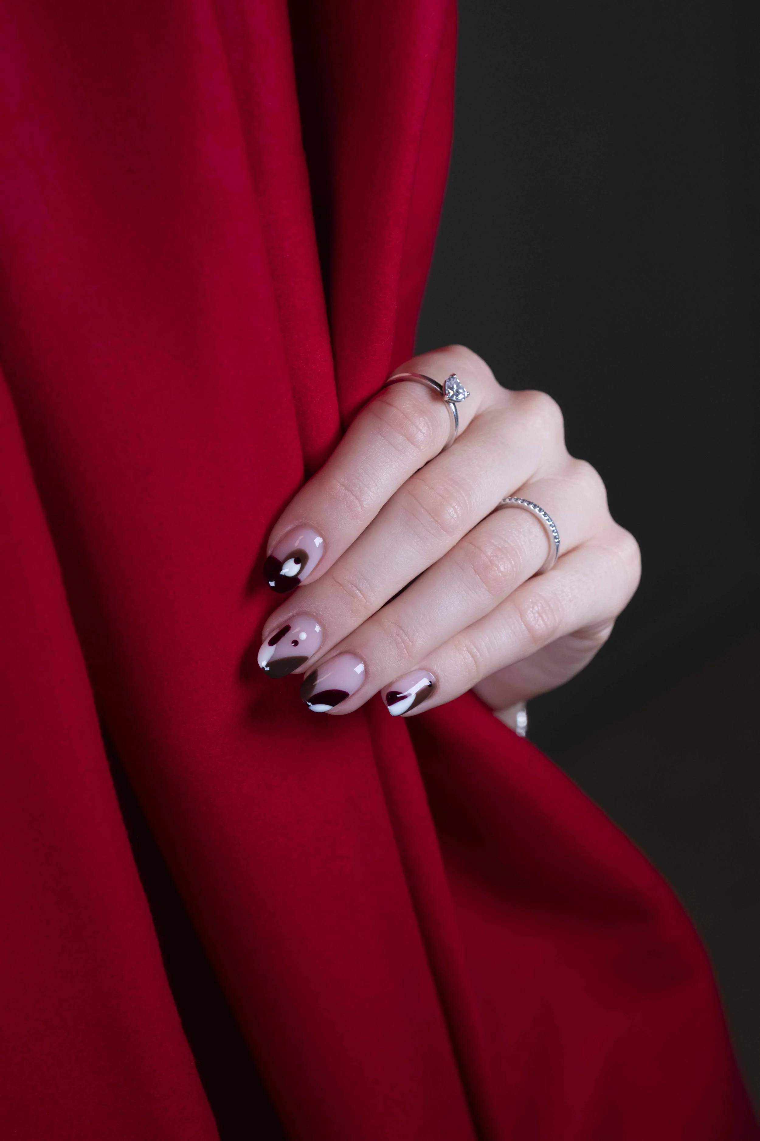 Mano con due anelli, uno con diamante a forma di cuore e l'altro con piccoli diamanti, che si poggia su un tessuto rosso.