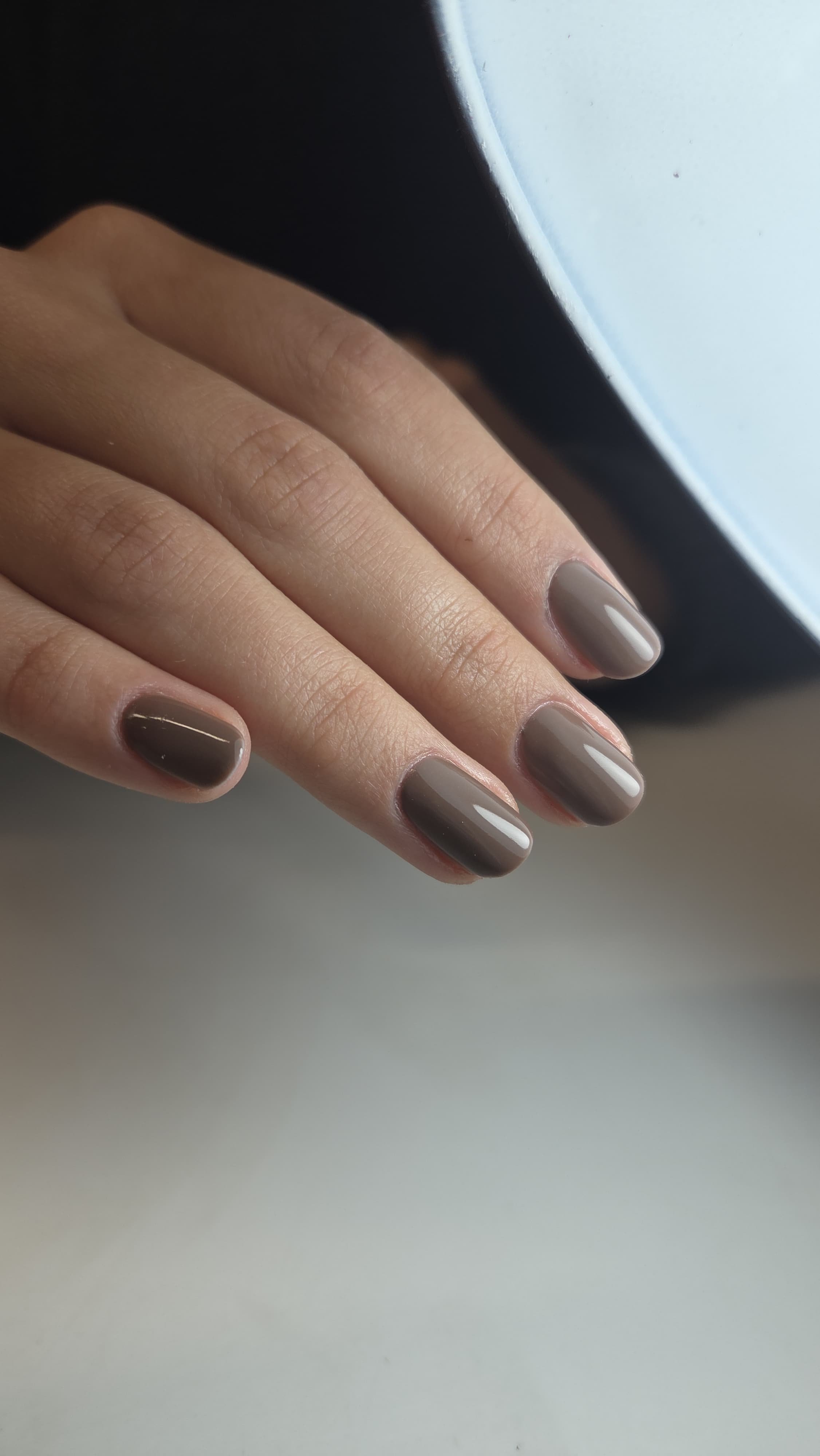 Un dito di mano femminile con unghie smaltate in tonalità di grigio e marrone chiaro, poggiato su una superficie chiara.