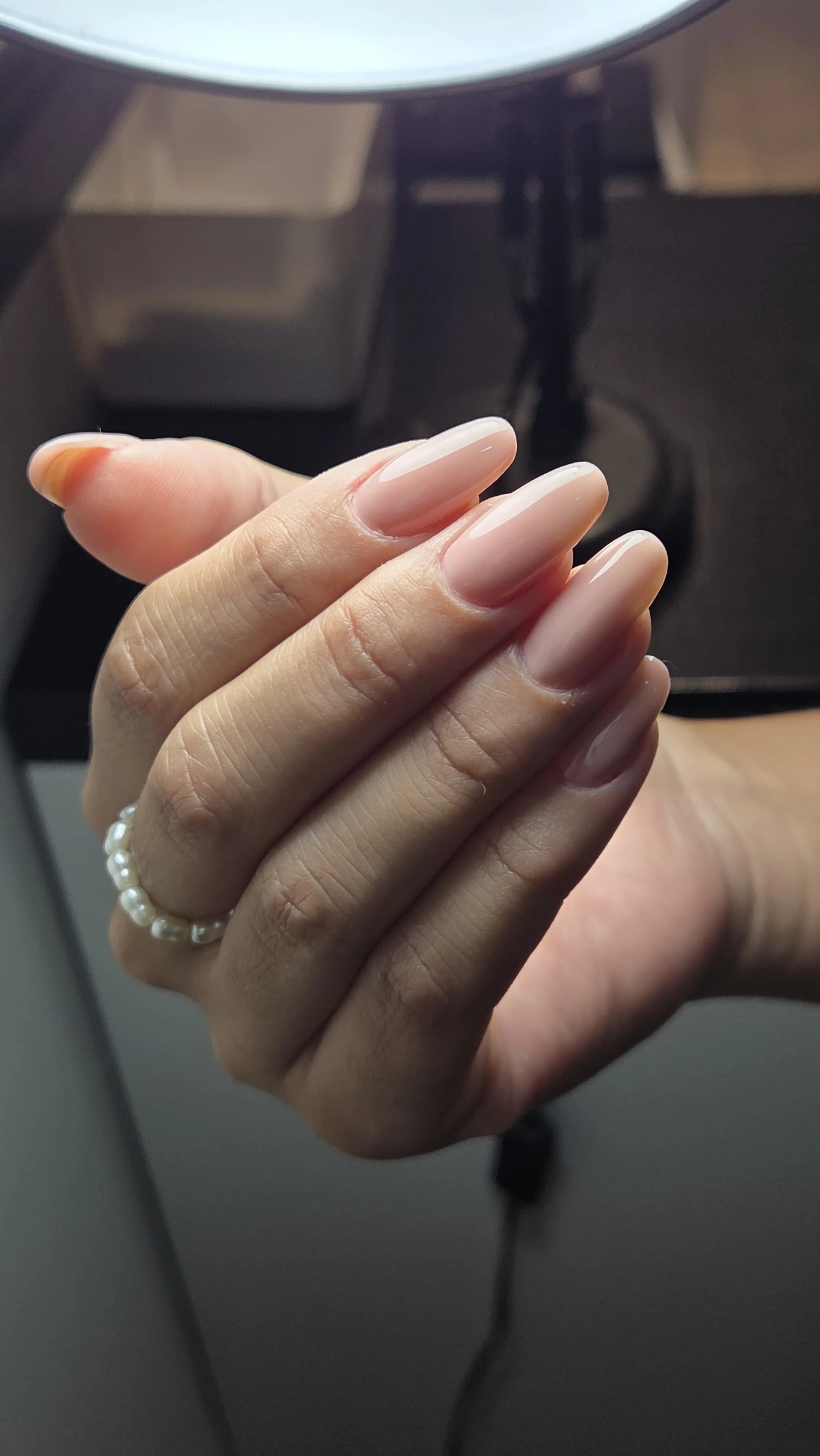 Mano con unghie curate e brief con smalto naturale, indossa un anello di perle
