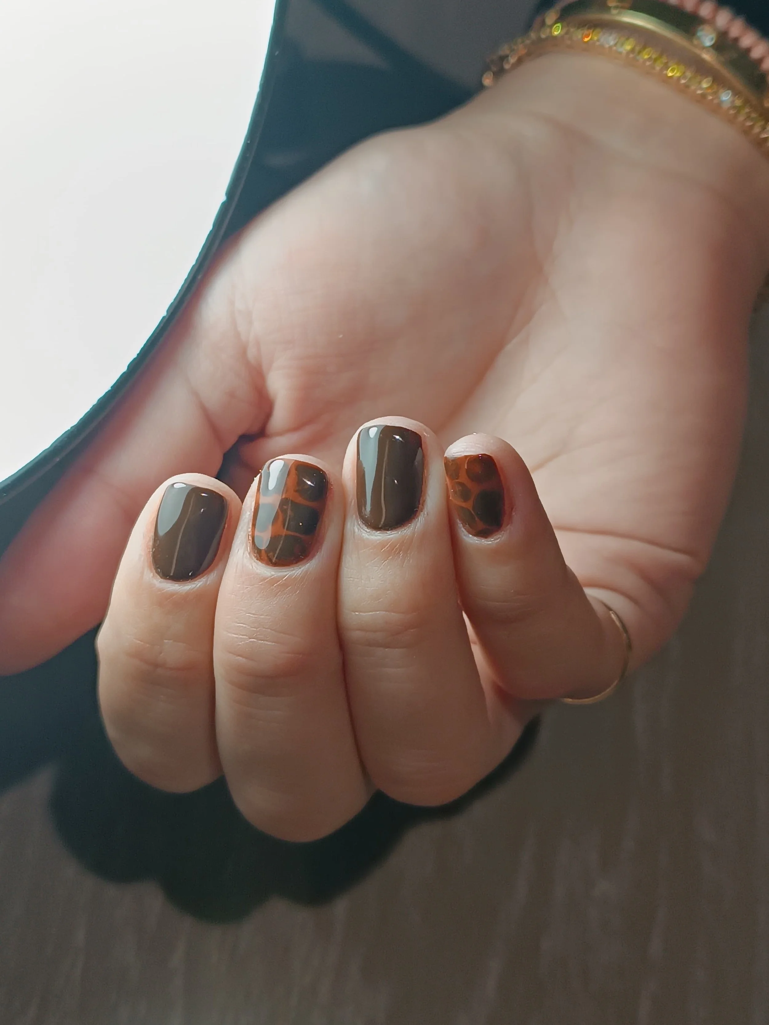 Immagine di una mano con unghie dipinte con design leopardato in toni marroni e neri, che tiene un telefono