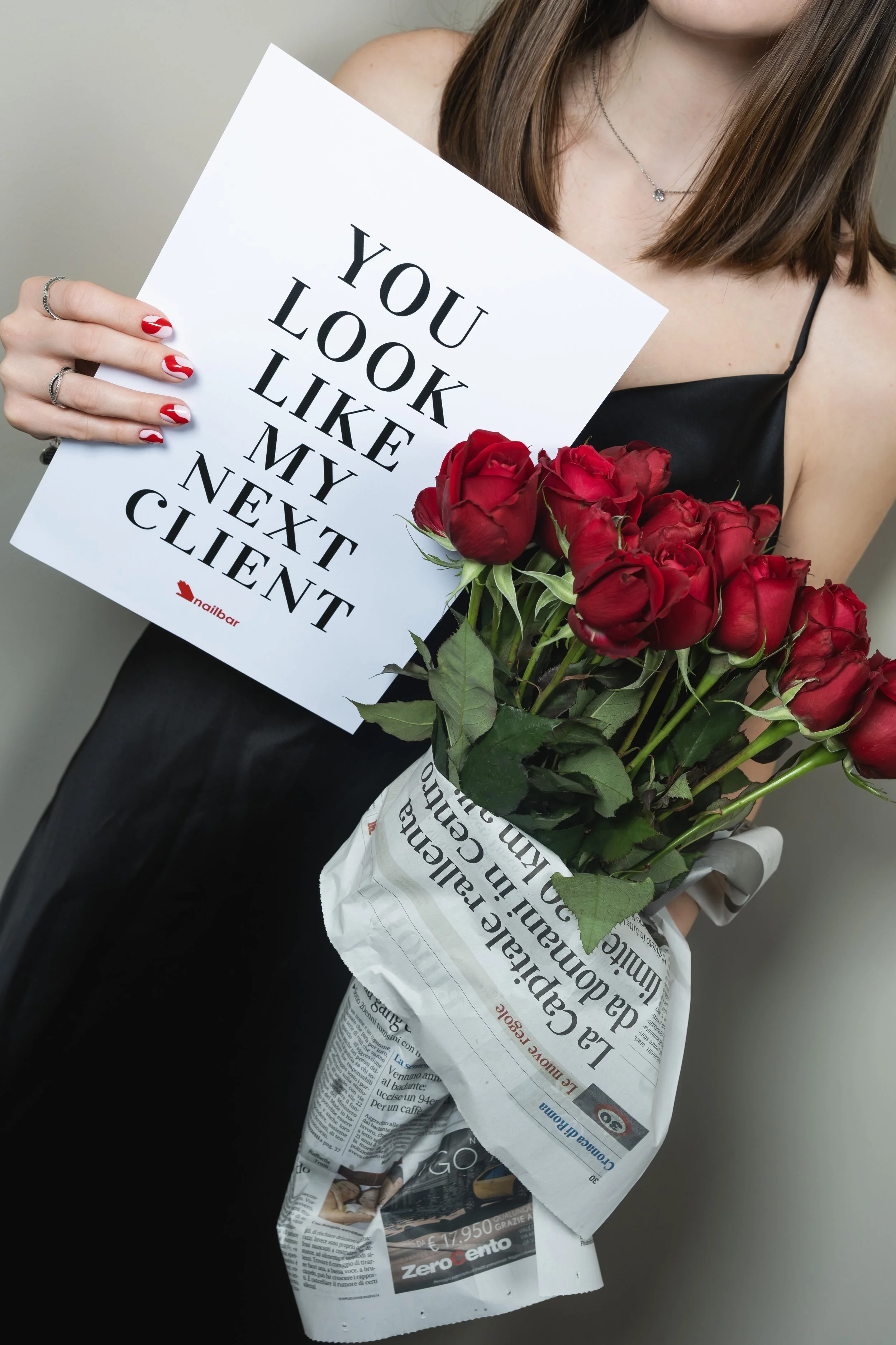 Una donna tiene un mazzo di rose rosse e un cartello con la scritta 'You look like my next client'.