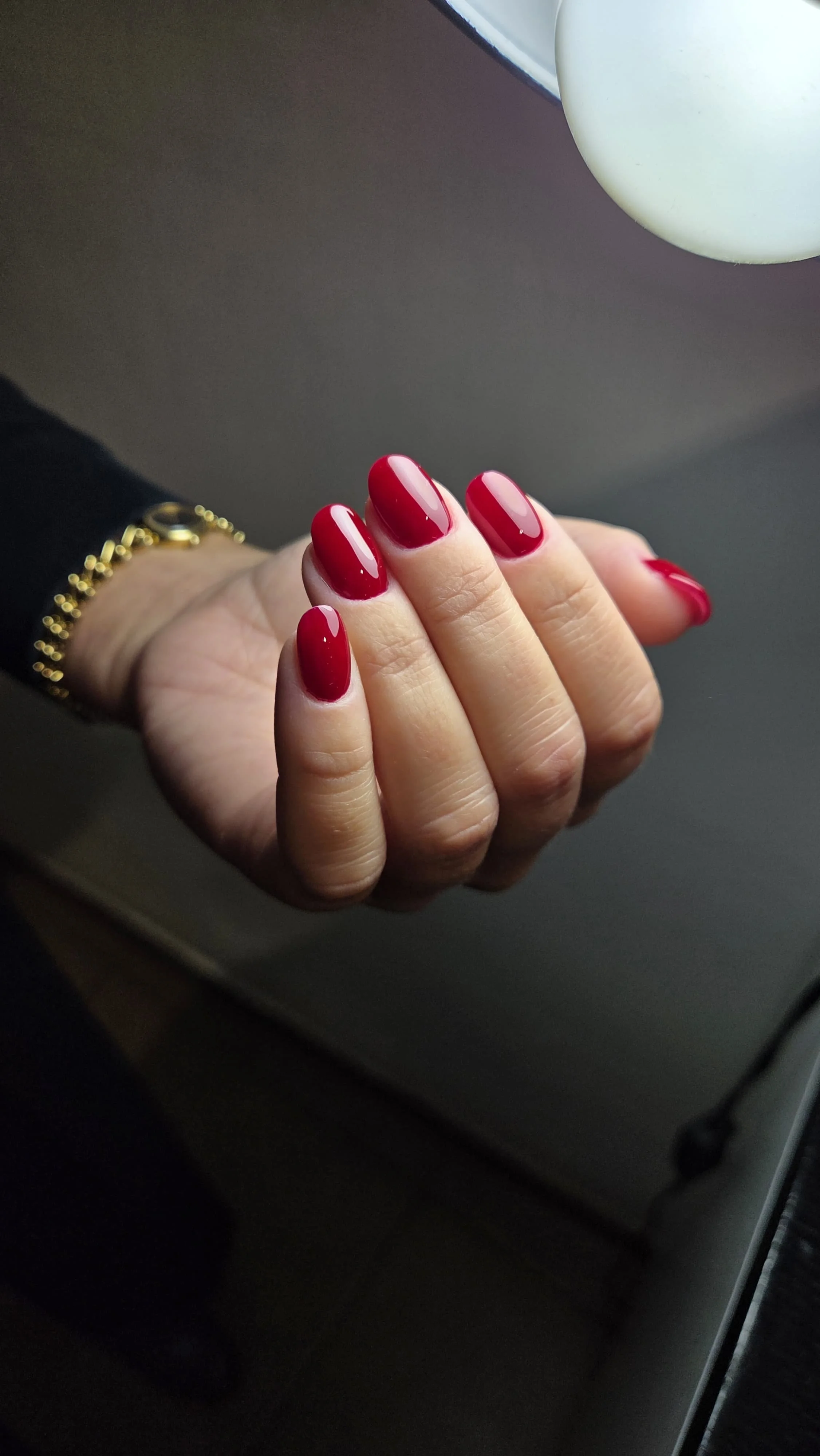 Un mano con unghie smaltate di rosso brillante appoggiata su una superficie con luce bianca.