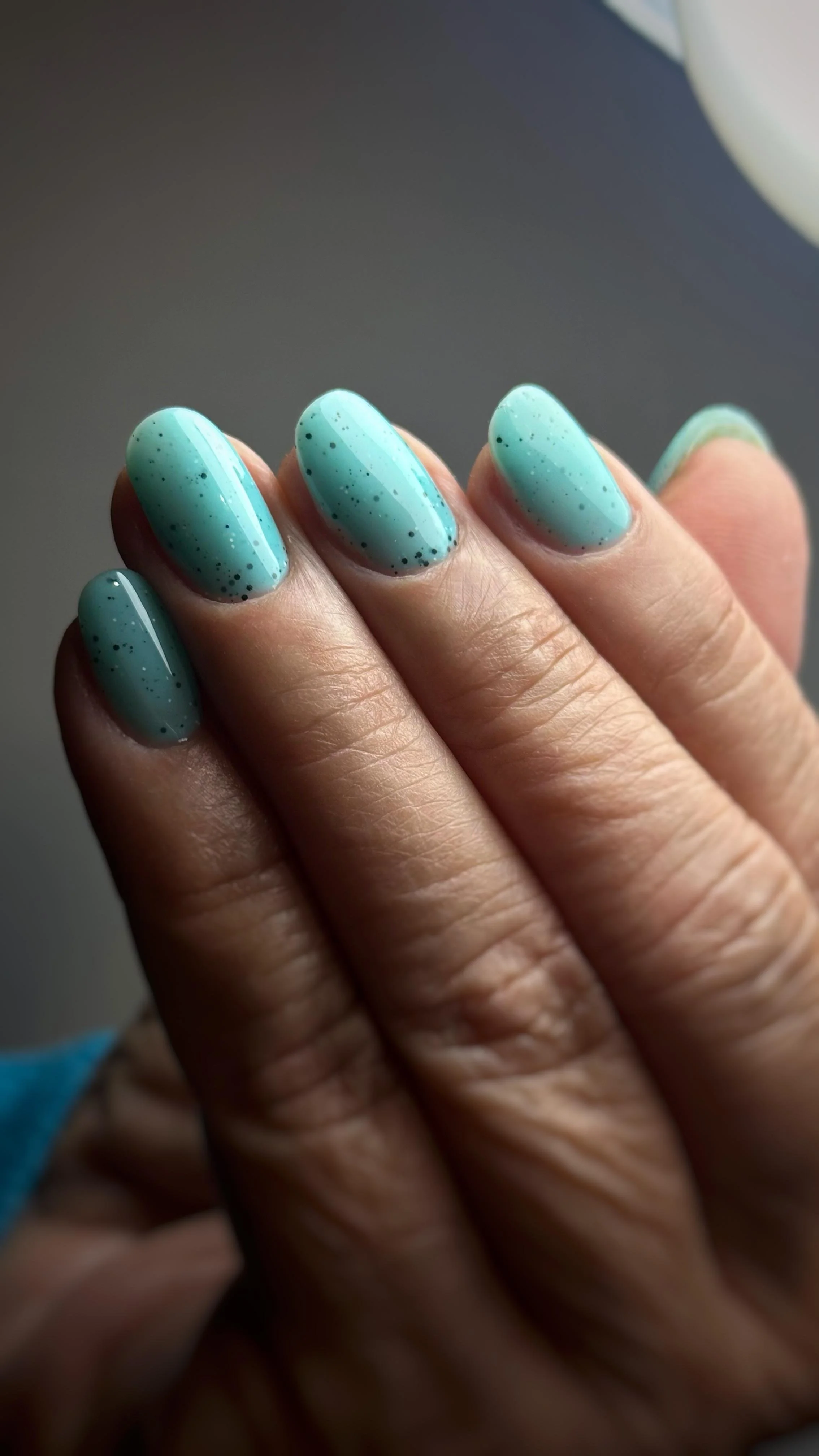 Unghie dipinte di un colore azzurro con piccole macchie nere.