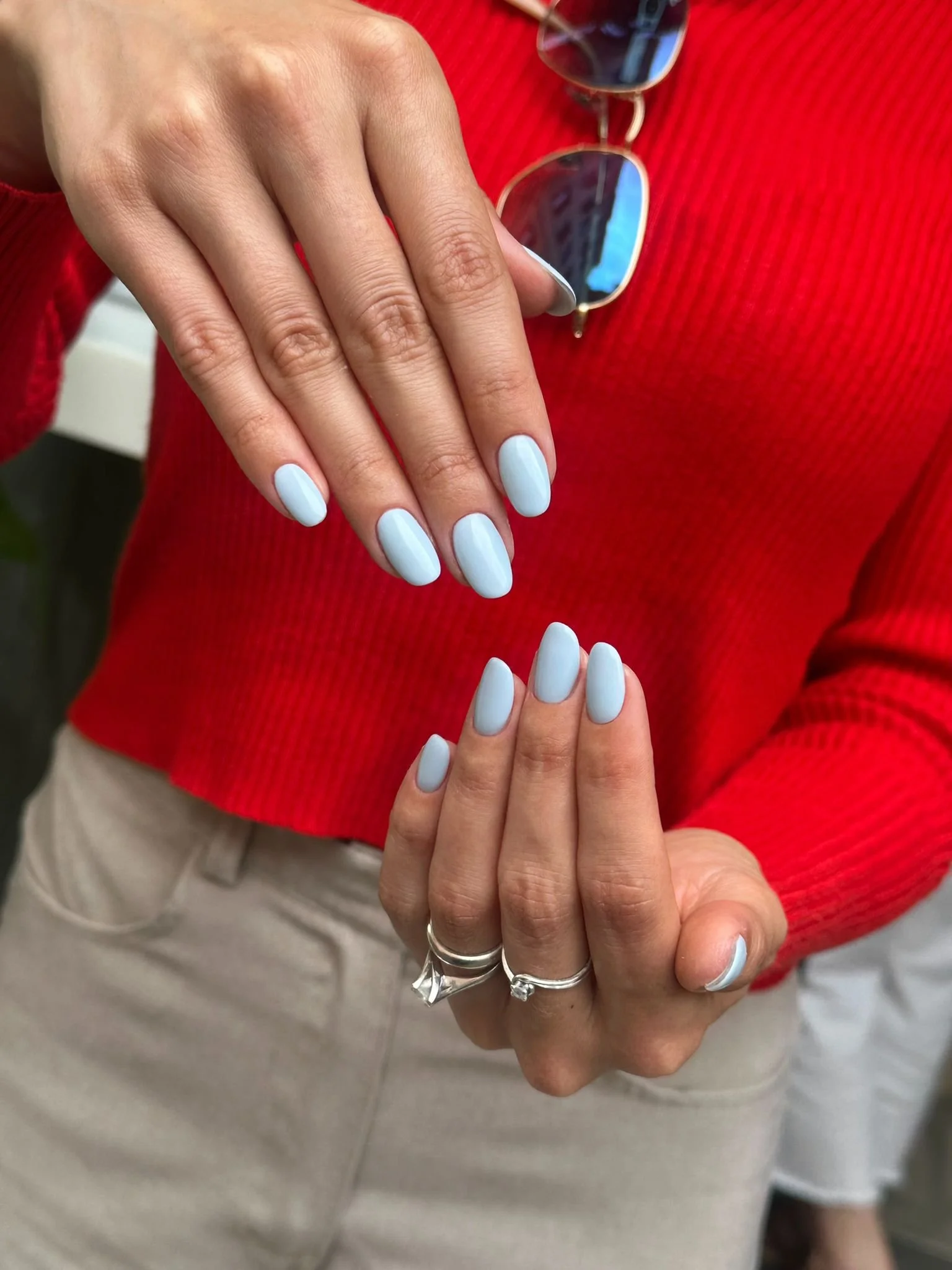 Due mani che mostrano unghie dipinte di azzurro, con uno sfondo di abbigliamento rosso e accessori metallizzati.