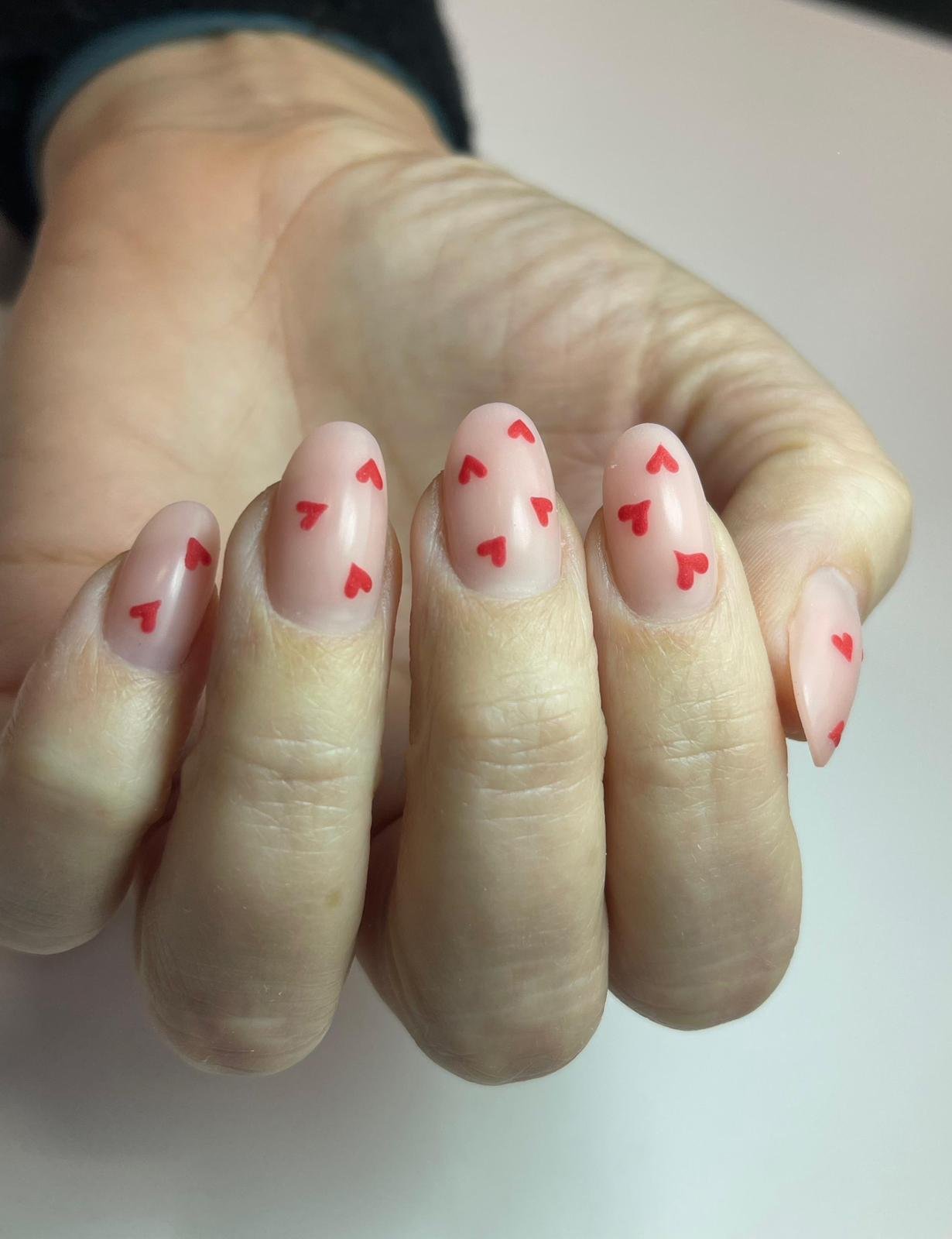 Unghie con decorazioni a cuoricino rosso su una mano