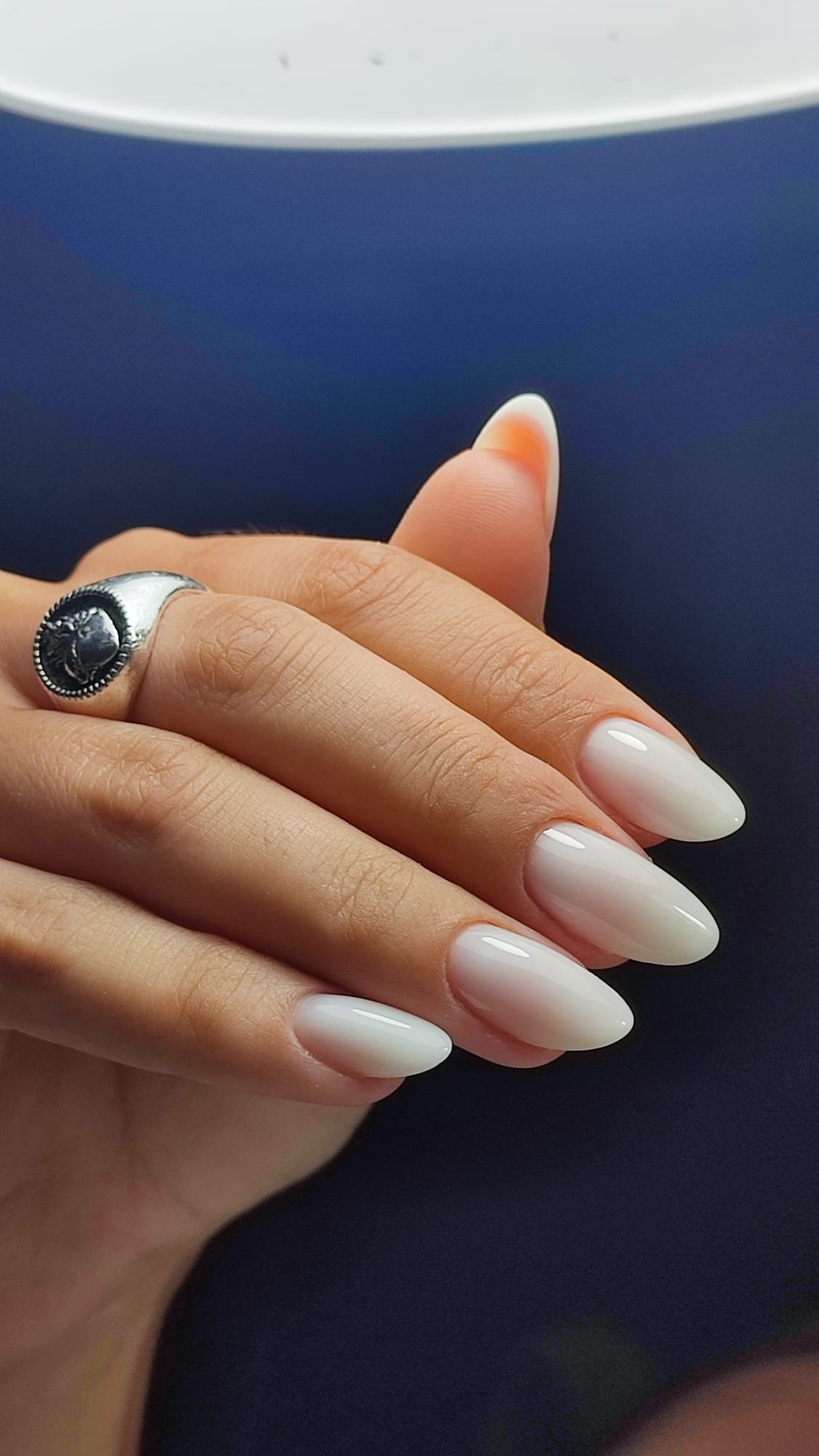 Mano con un anello argentato con motivo a testa di leone e unghie curate con smalto color avorio