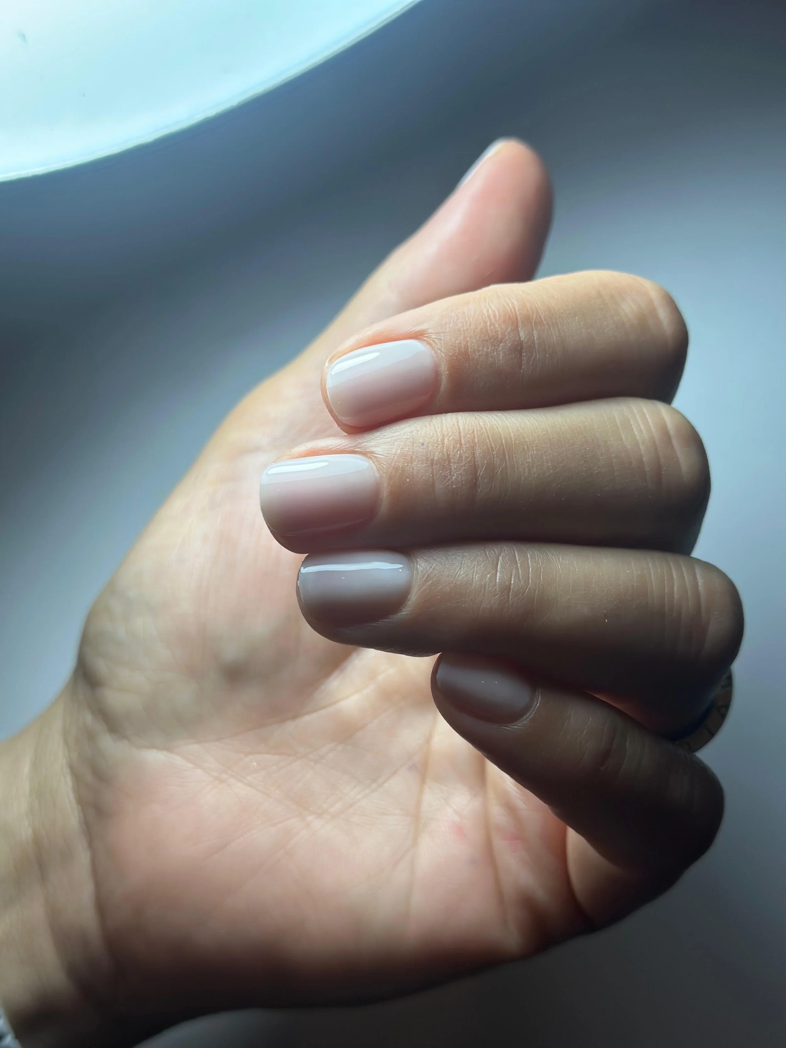 Mano con unghie curate e smaltate di colore nude, avvolta da luce naturale