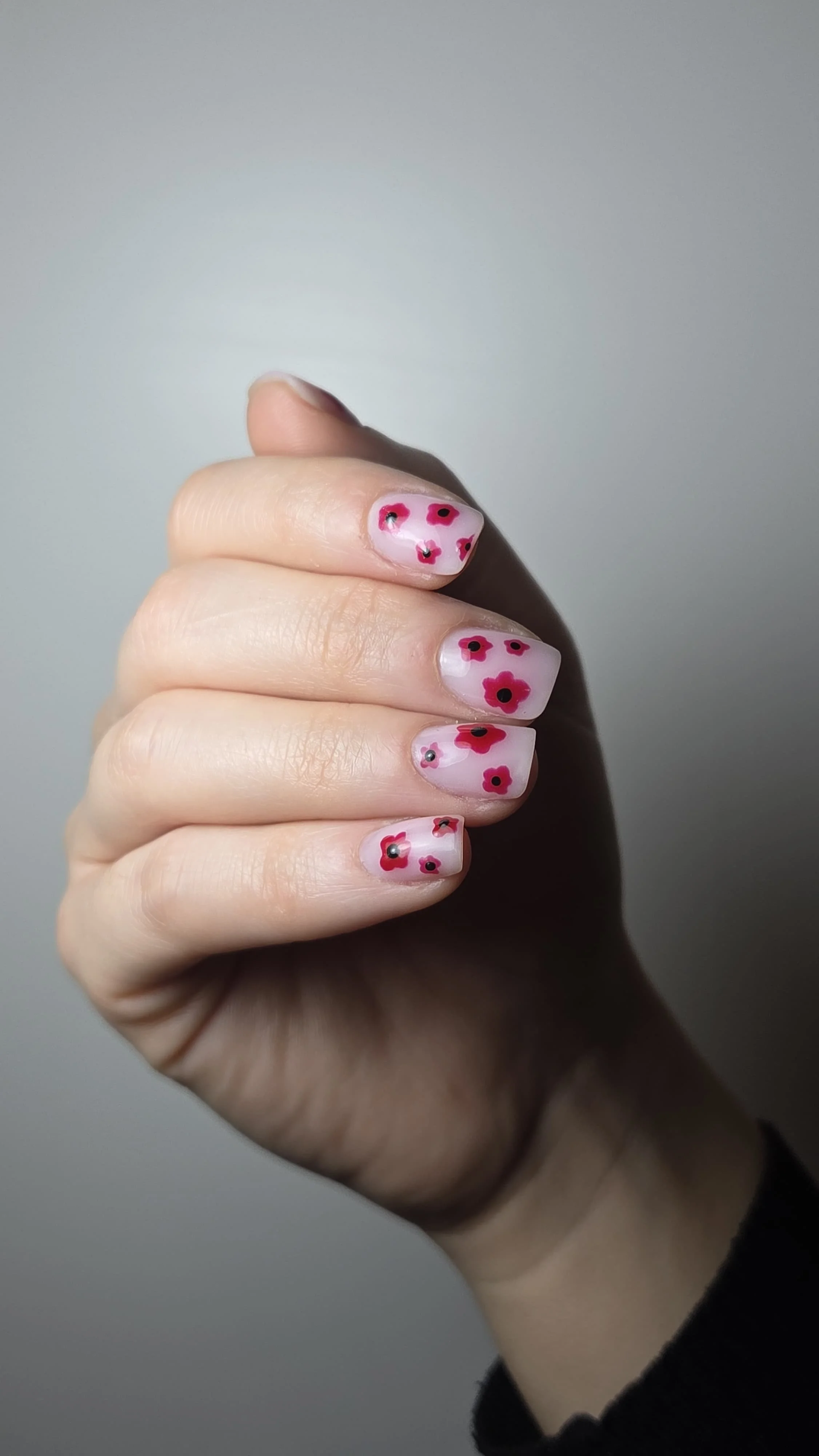 Unghie dipinte con un design di fiori rossi e neri su uno sfondo rosa chiaro.