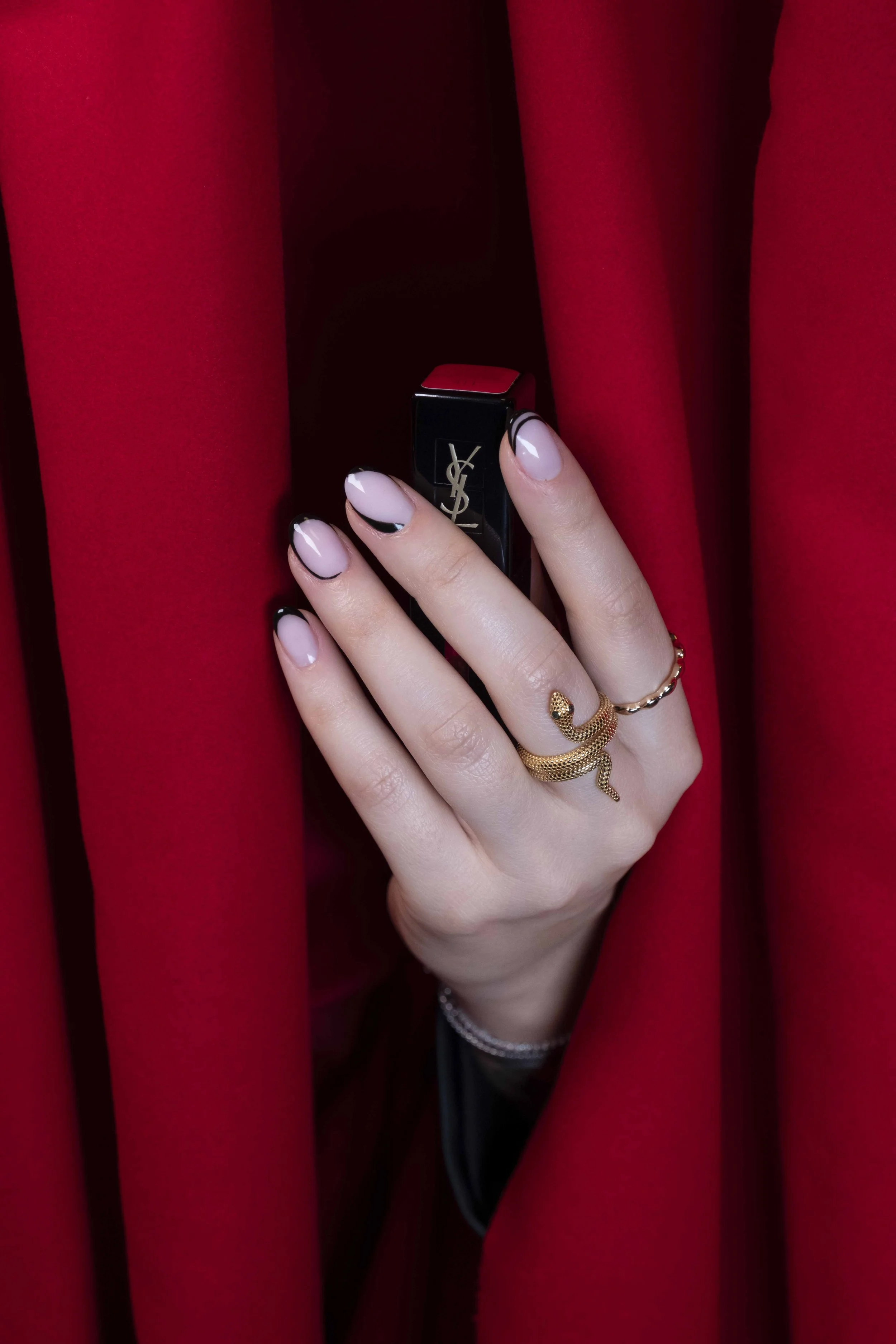 Mano con un rossetto di Yves Saint Laurent tra le tende rosse.
