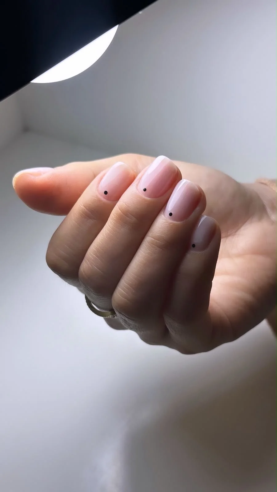 Un'unghia con smalto chiaro e piccoli punti neri come decorazione.