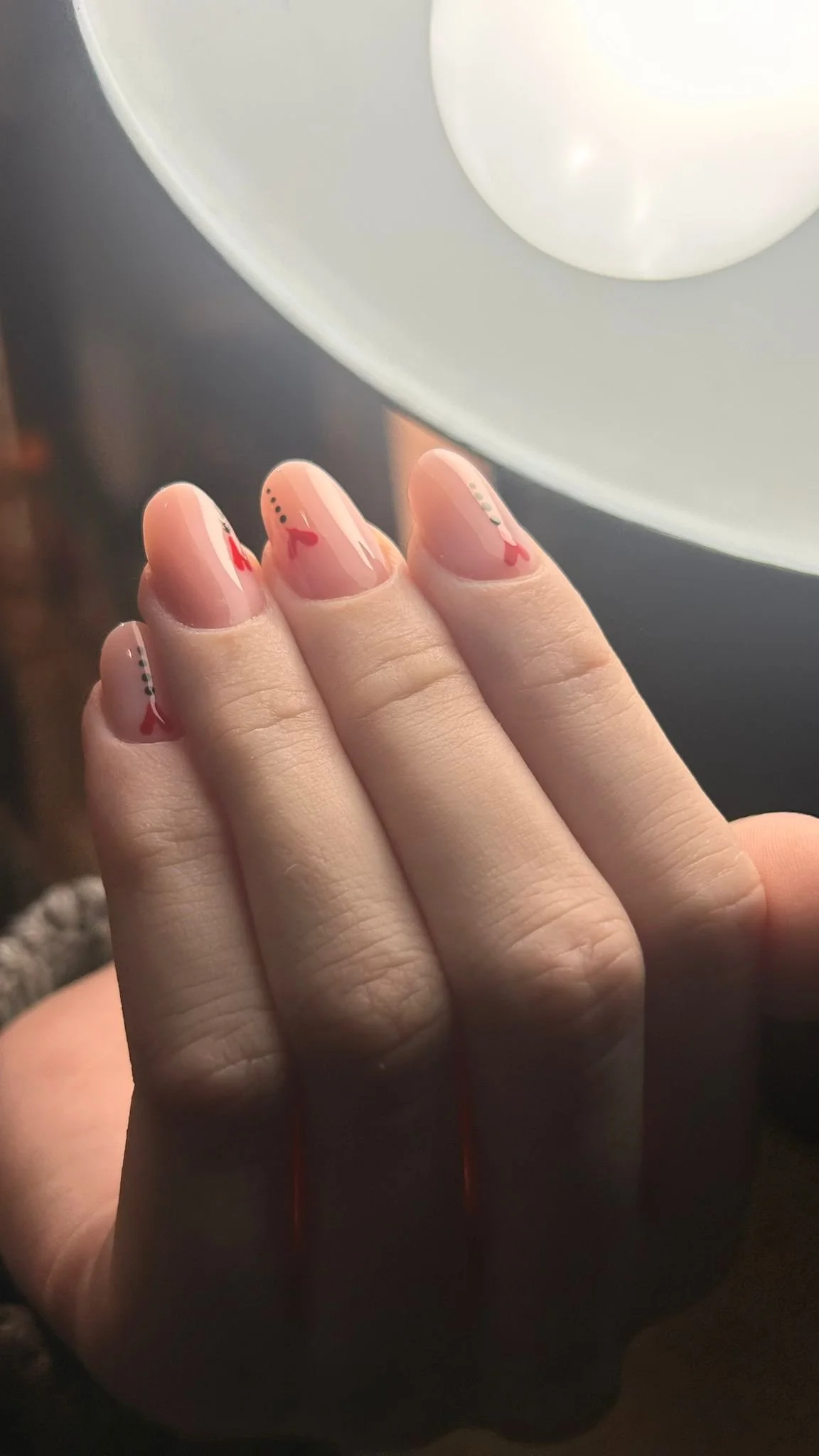 Unghie decorate con disegni di cuori e punti, visibili sulle dita di una mano. Sullo sfondo, una lampada bianca.