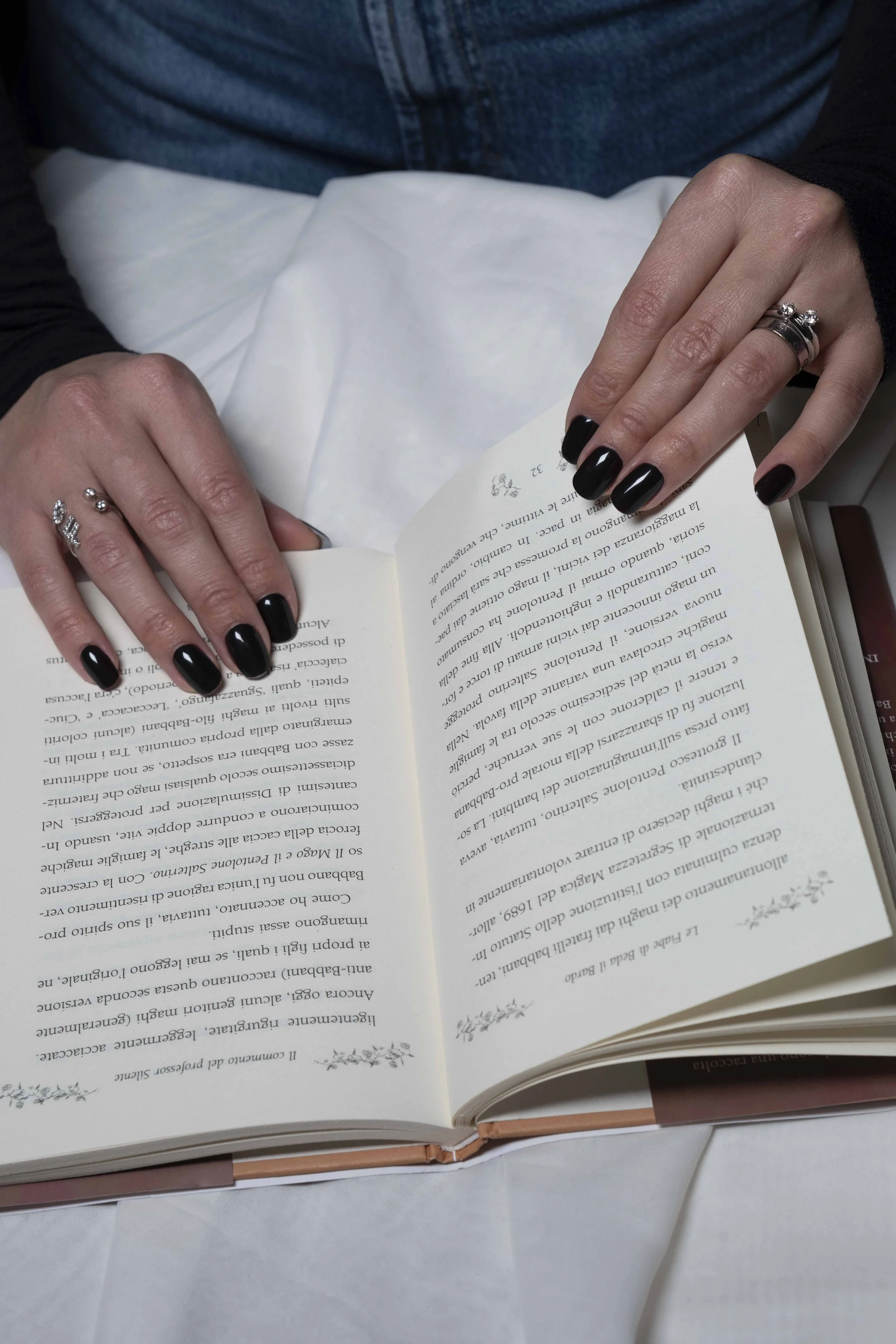 Mani con unghie nere e anelli che tengono aperto un libro con testo in italiano.