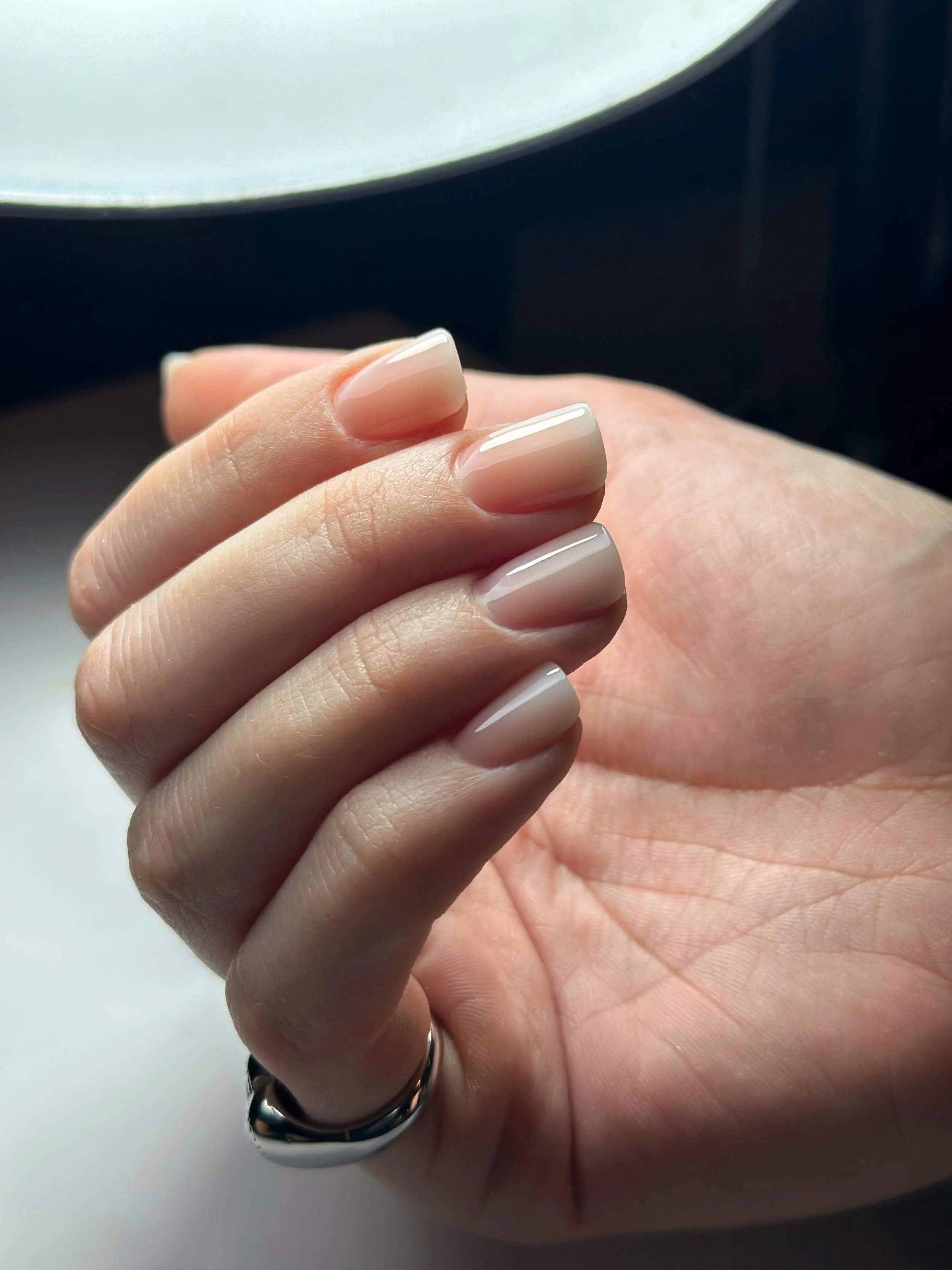 Una mano con unghie curate e smaltate di colore nude, indossa un anello in argento, in primo piano.