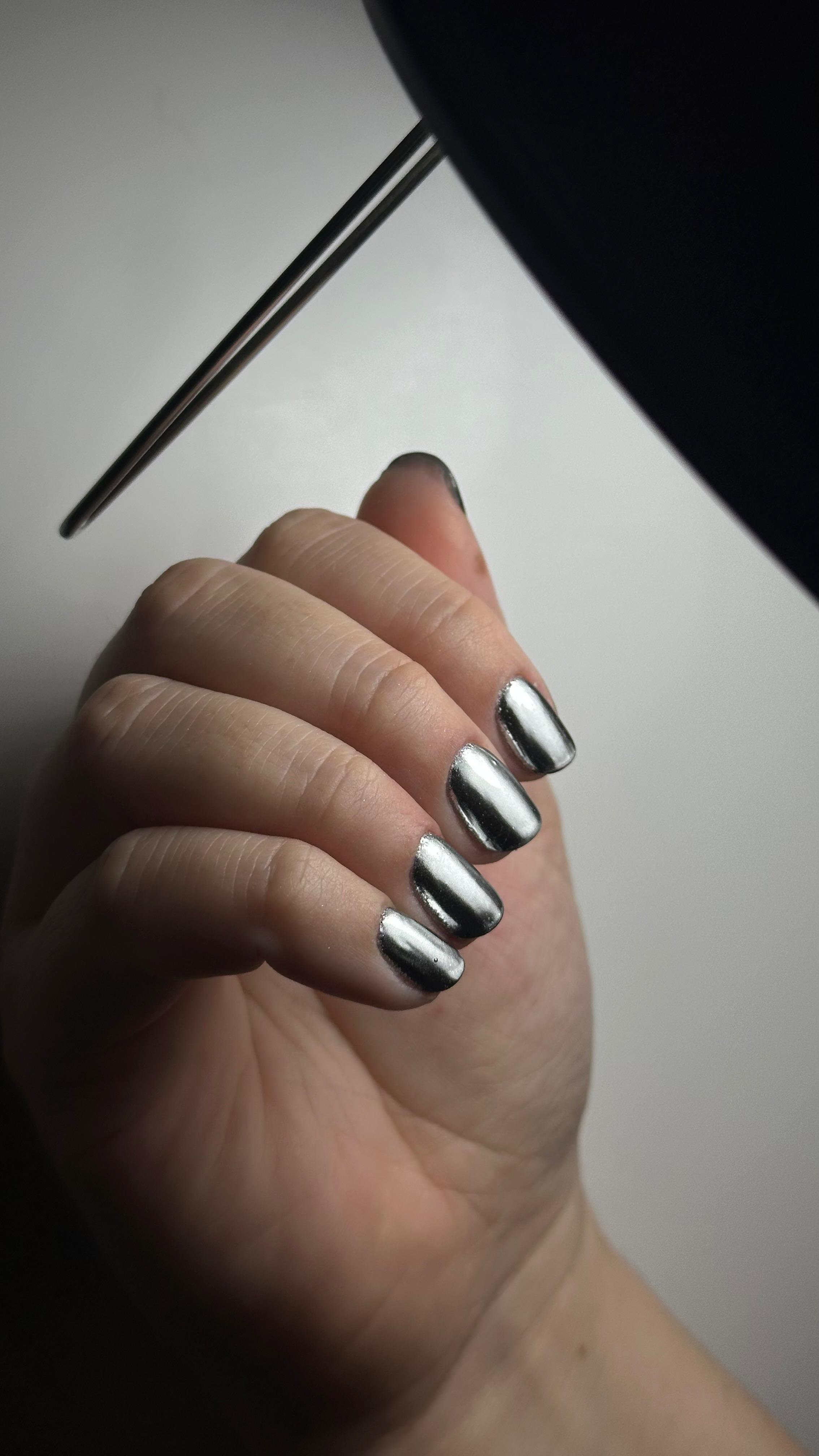 Mano con unghie dipinte di colore argento scuro, tenendo un telefono nero.