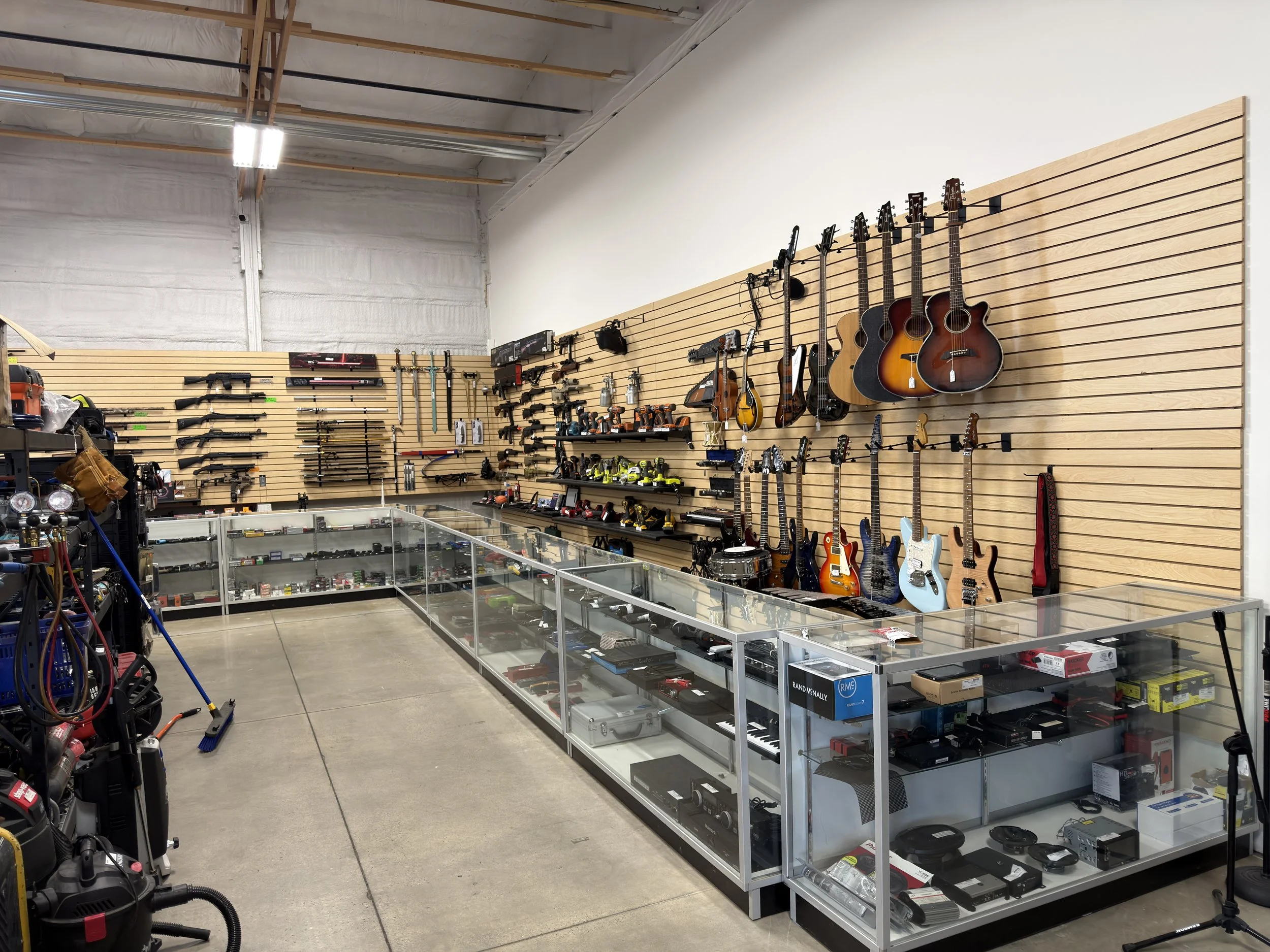 A retail store section displaying guitars hanging on the wall, with various other items and tools on glass display cases and shelves.