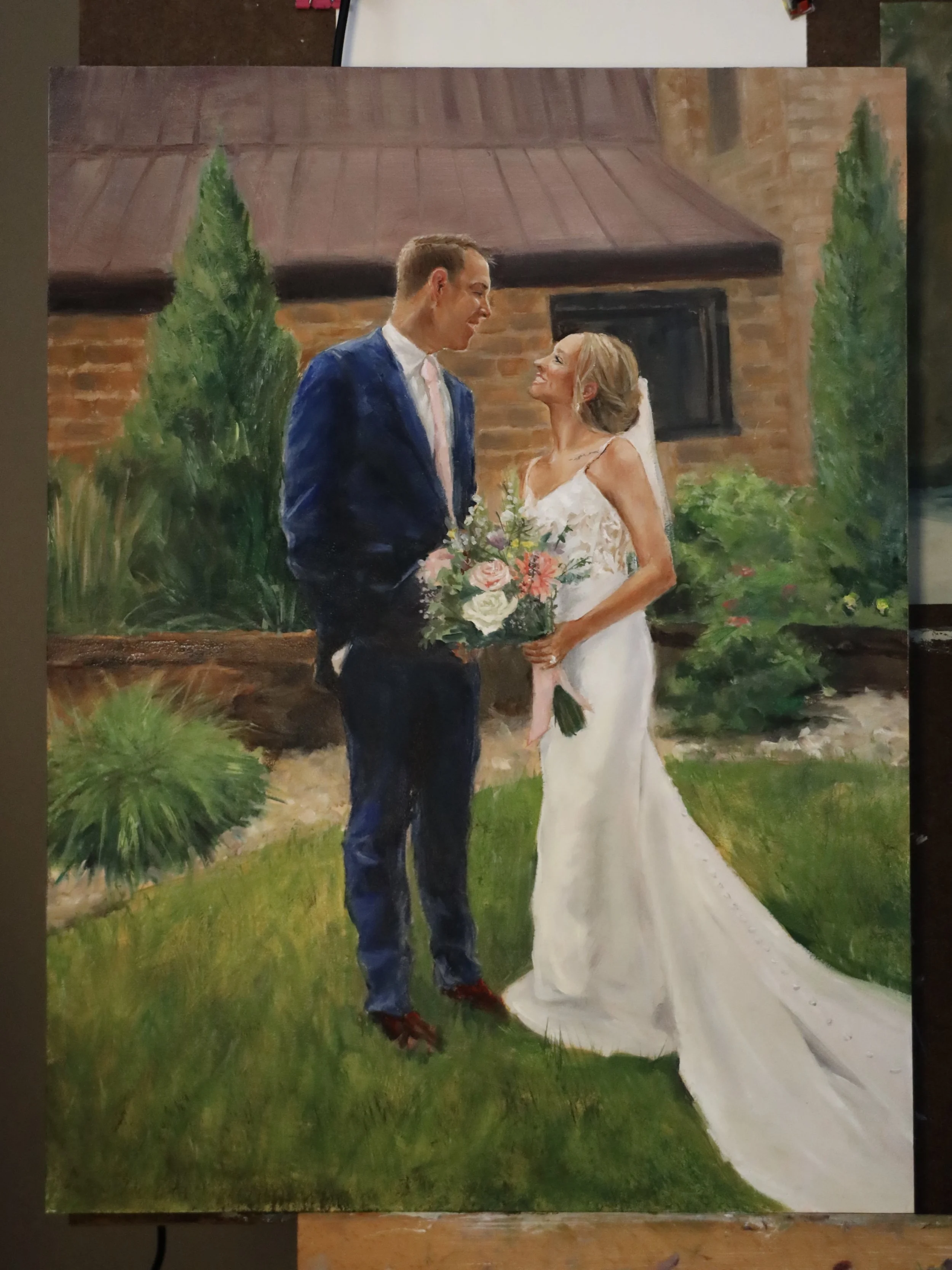A painting of a wedding scene showing a bride and groom standing outdoors in front of a brick building surrounded by greenery, gazing at each other and smiling.