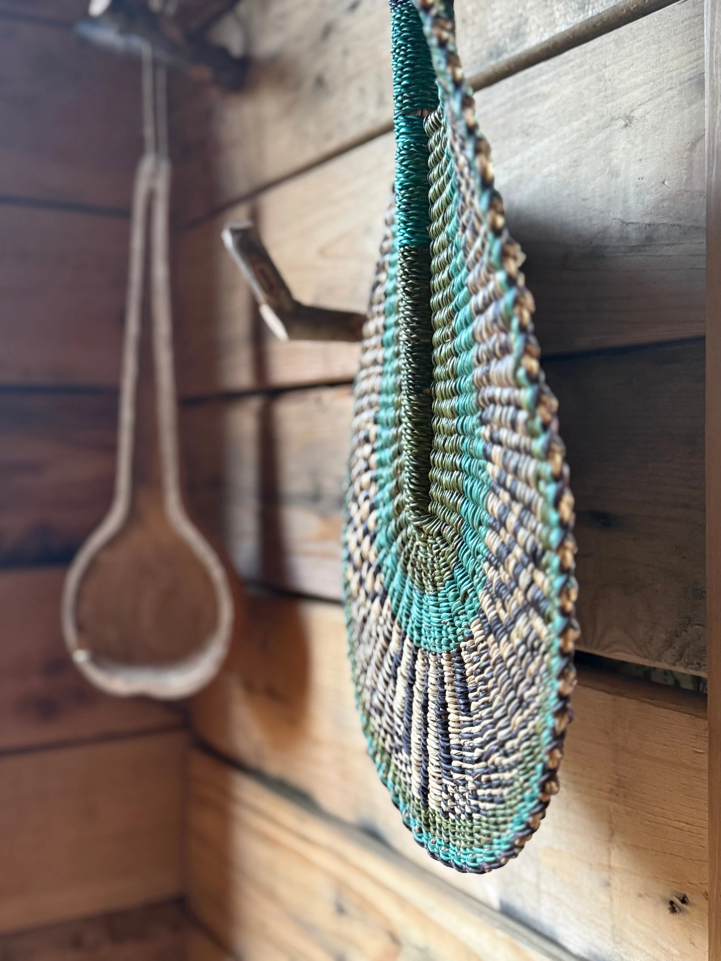 Colorful woven straw bag hanging on wooden slats inside a rustic wooden space.