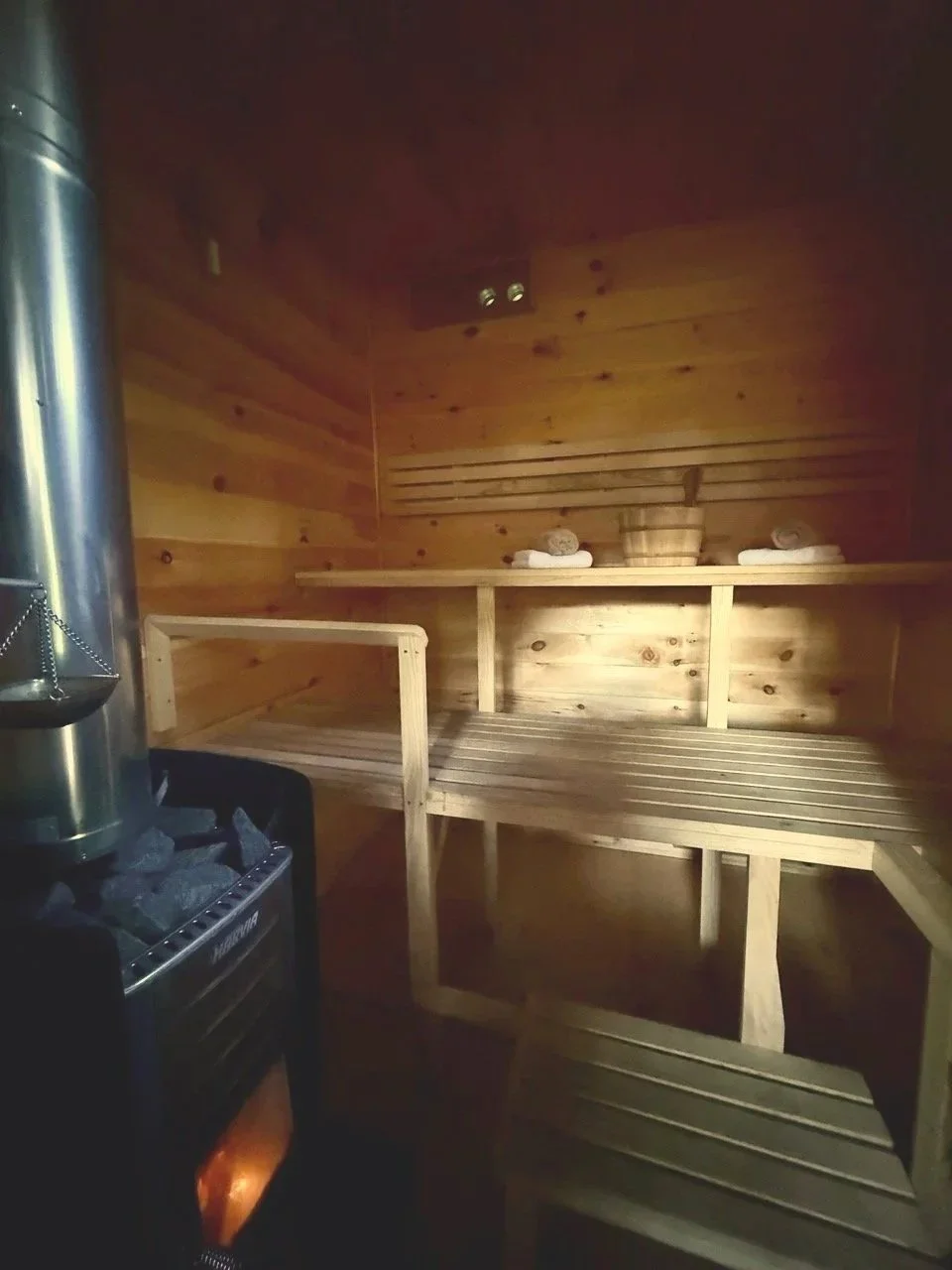 Wooden sauna interior with bench seating, towels, and a sauna stove with rocks.