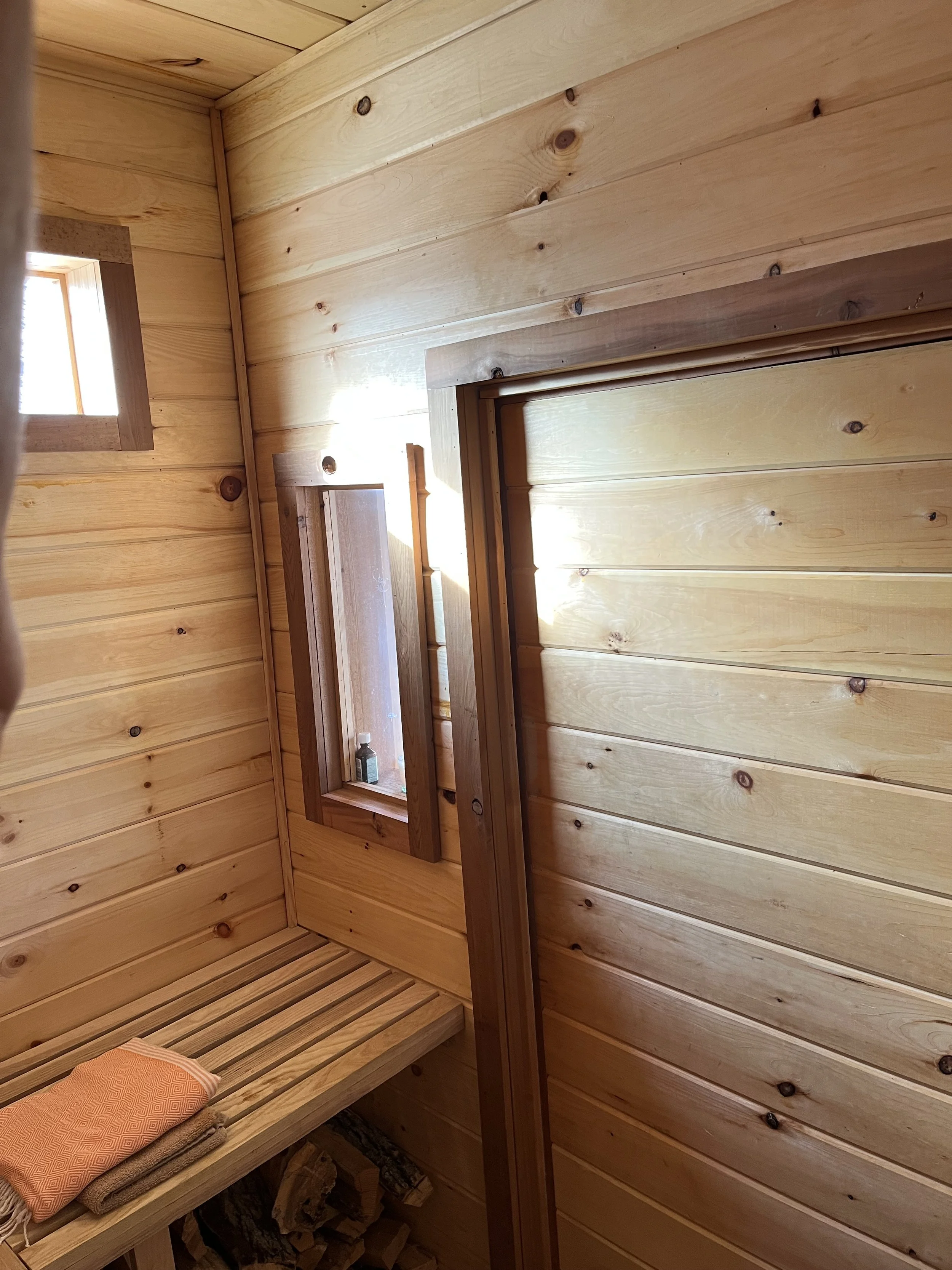 Interior of a small wooden sauna with a wooden bench, wooden walls, and a small window letting in natural light.