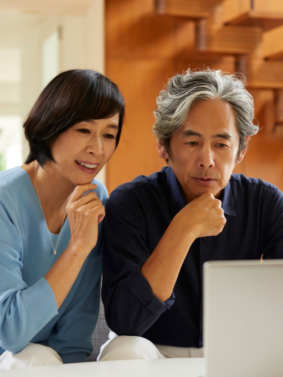 A middle-aged woman and man look at a laptop together in a home setting, appearing engaged.