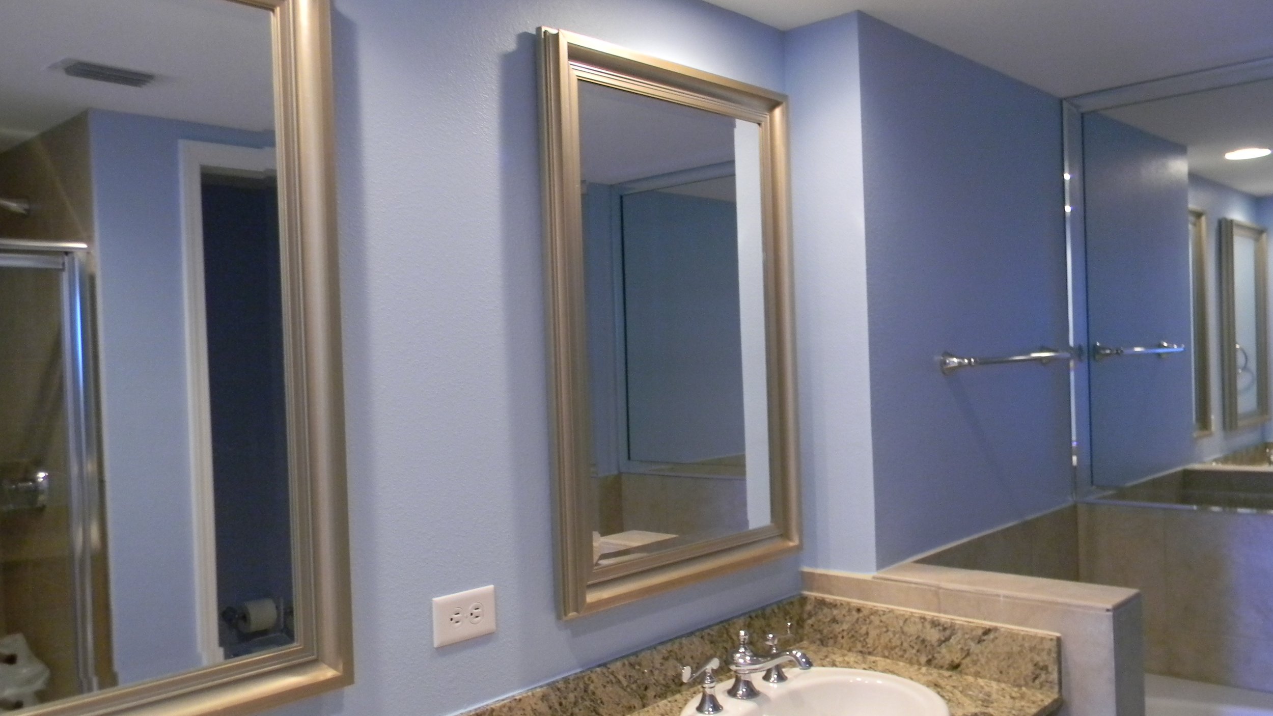Bathroom with two mirrors, a blue wall, and a granite countertop with a sink.