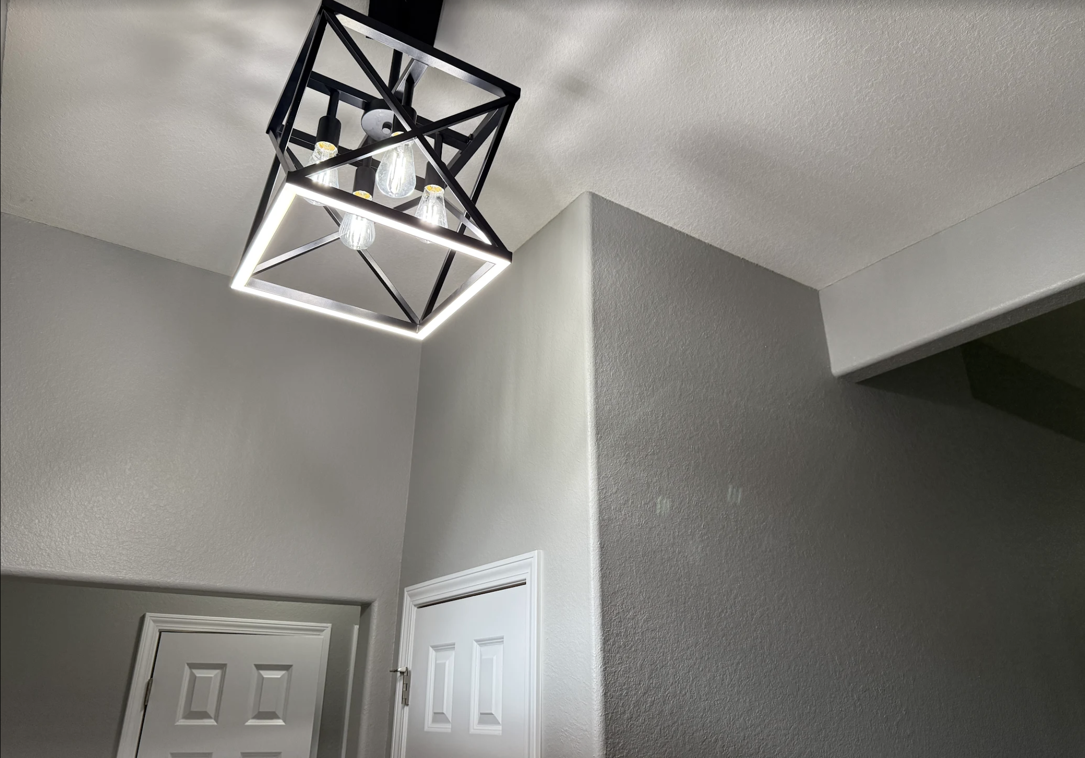 Ceiling light fixture with black geometric frame and multiple exposed Edison-style bulbs in a modern interior room.