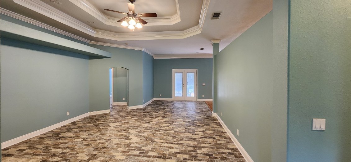 Empty living room with light green walls, a ceiling fan with light, and double glass doors at the end.