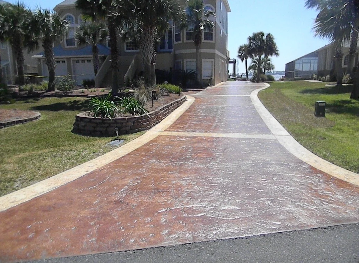A curved brick pathway in front of residential buildings with palm trees and grass on either side, leading to the water in the distance.