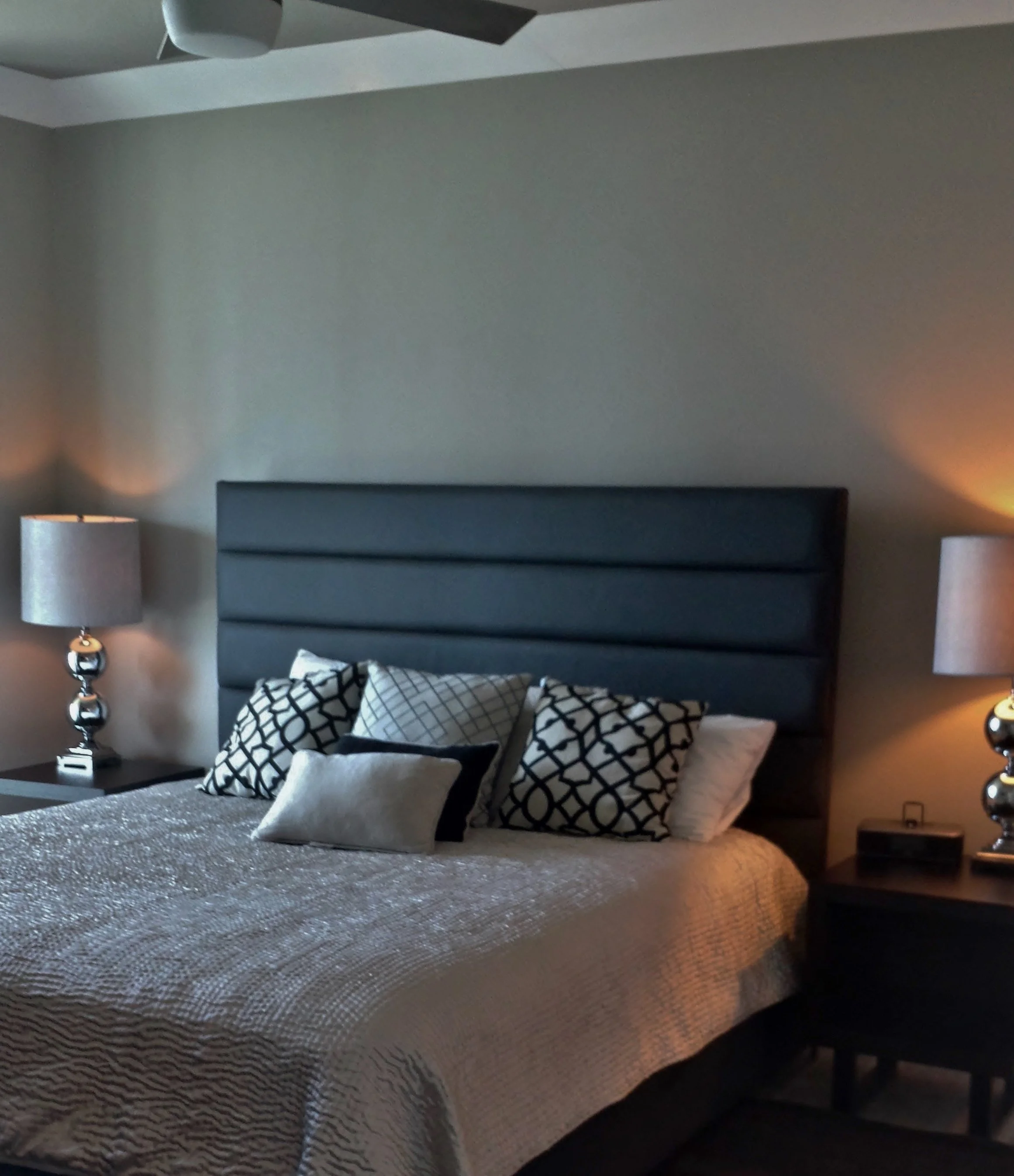 A bedroom with a bed, pillows, nightstands, lamps, and a gray upholstered headboard, illuminated with soft lighting.