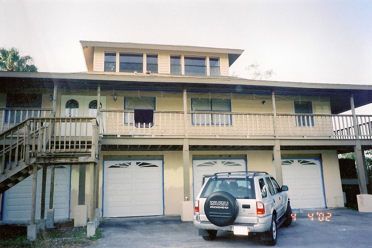 Multi-story residential building with a garage and a parked Isuzu Rodeo SUV in front.