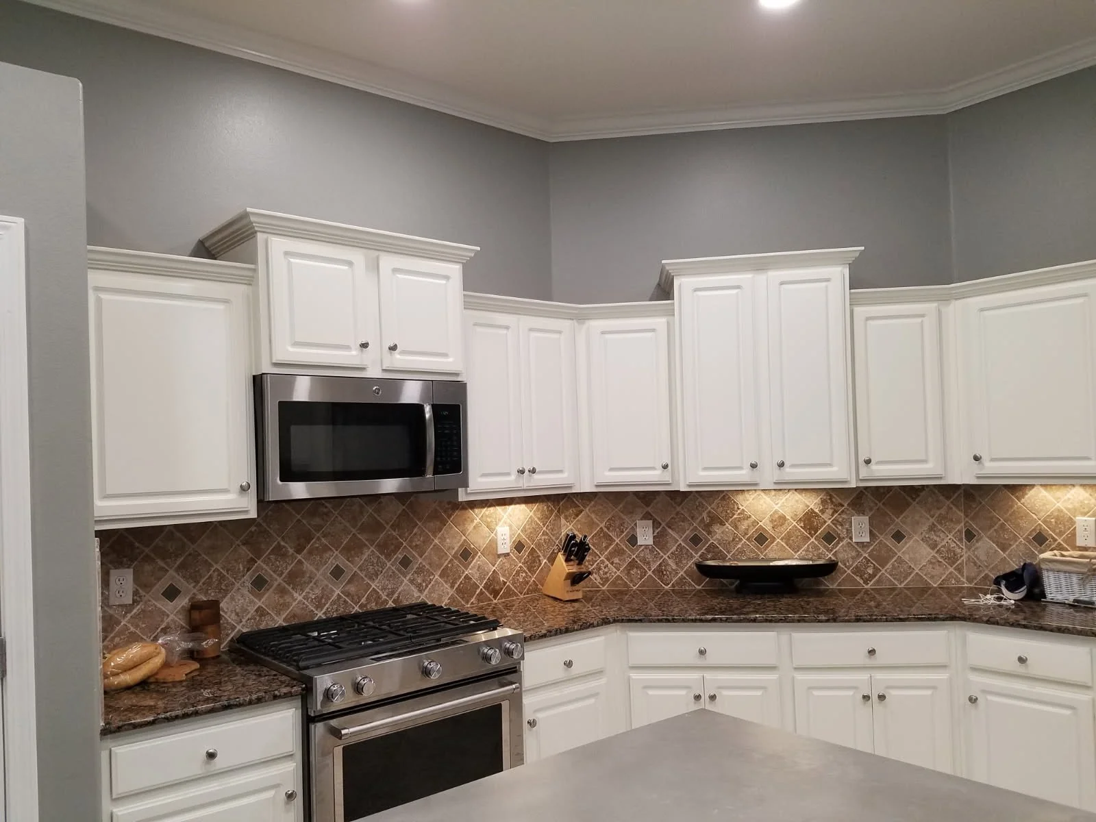 Kitchen with white cabinets, a microwave, a stove, and a granite countertop, beige tiled backsplash, and gray walls.