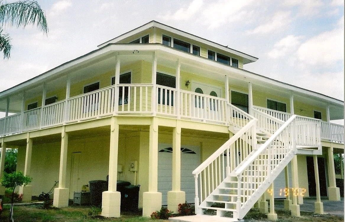 Beach Home Restoration Showing repaint with cheery yellow color and beautiful crisp white detailing on railings soffits stairwell doors window trim and garage doors