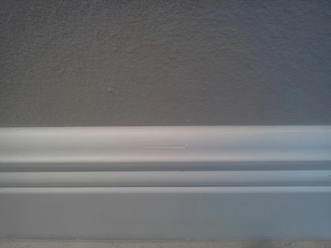 Close-up of a white baseboard against a textured gray wall.