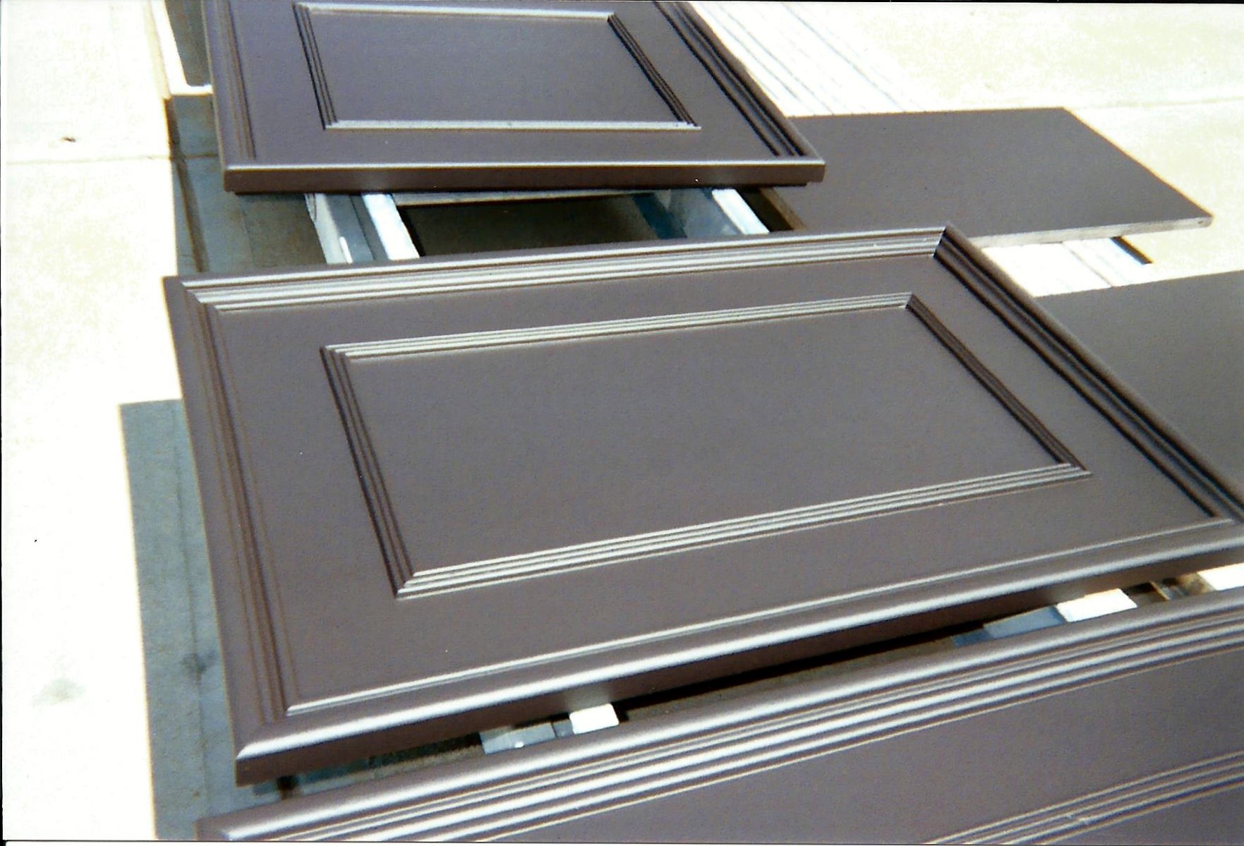 Multiple brown cabinet doors with decorative molding laid flat on a surface in an outdoor setting.