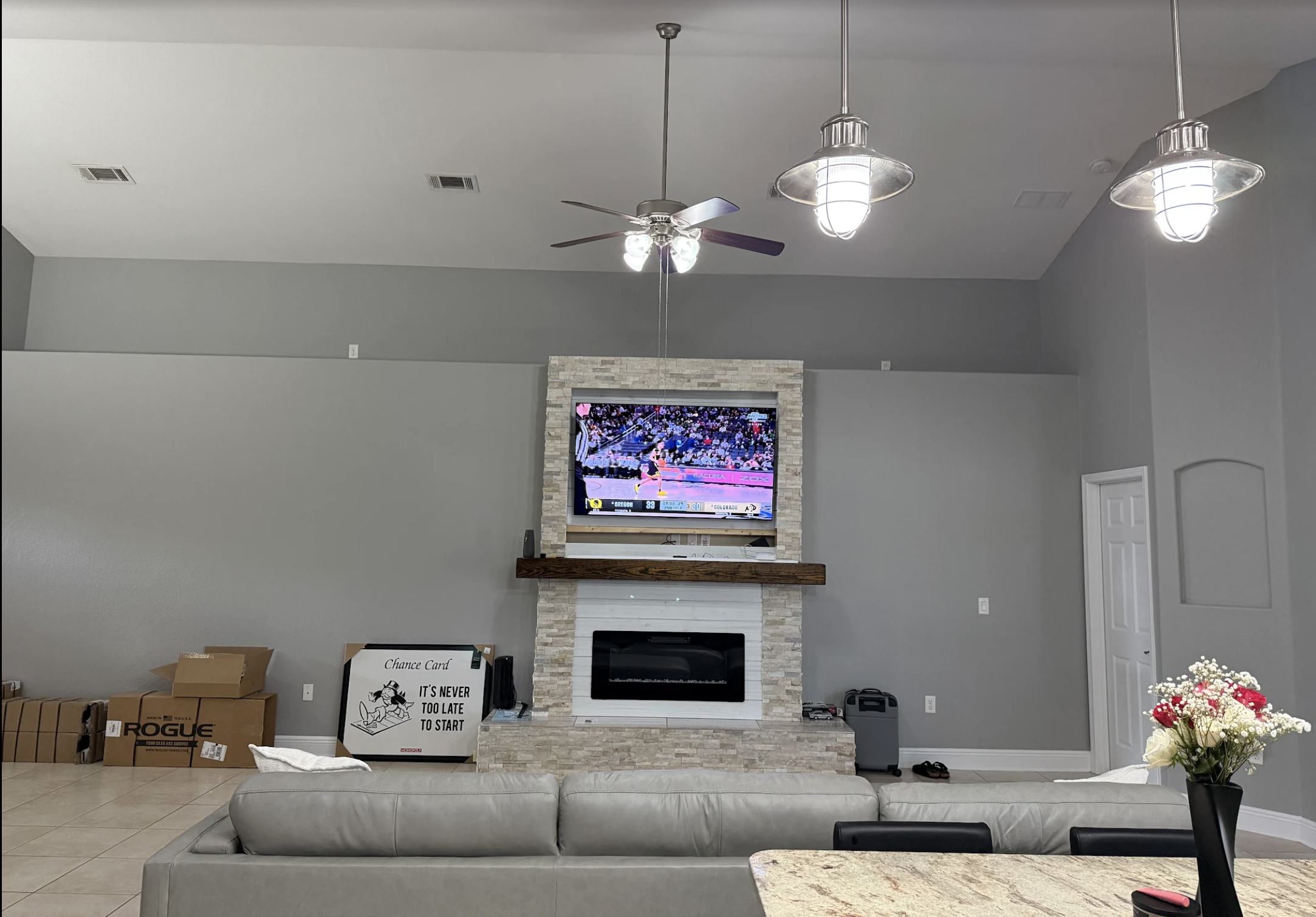 Living room with a gray fireplace, TV, ceiling fan, pendant lights, a couch, and boxes in the corner.