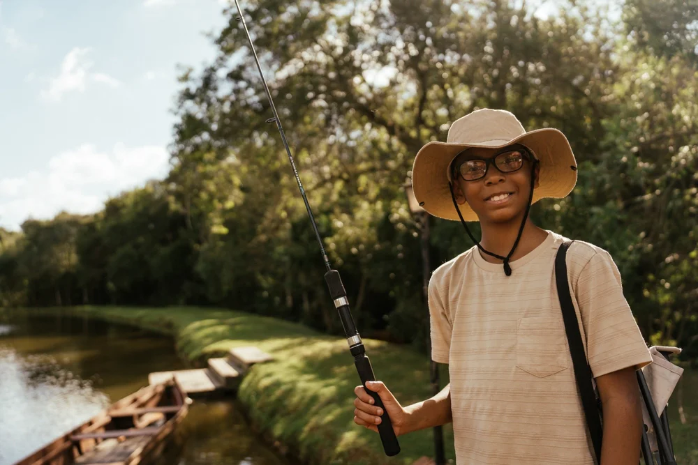 Boy smiling with a fishing rod by a pond